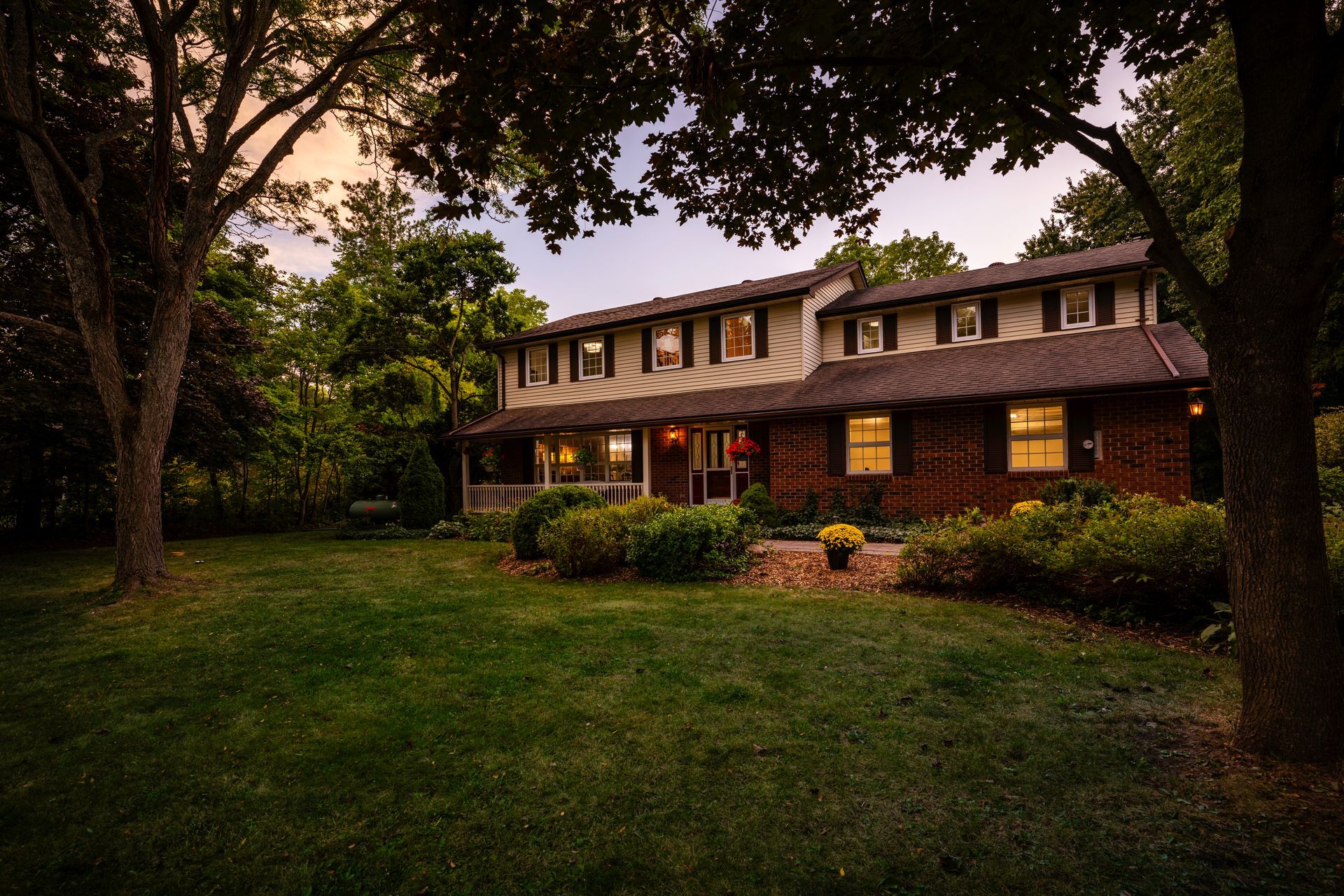 A large brick house with a large lawn and trees in front of it.