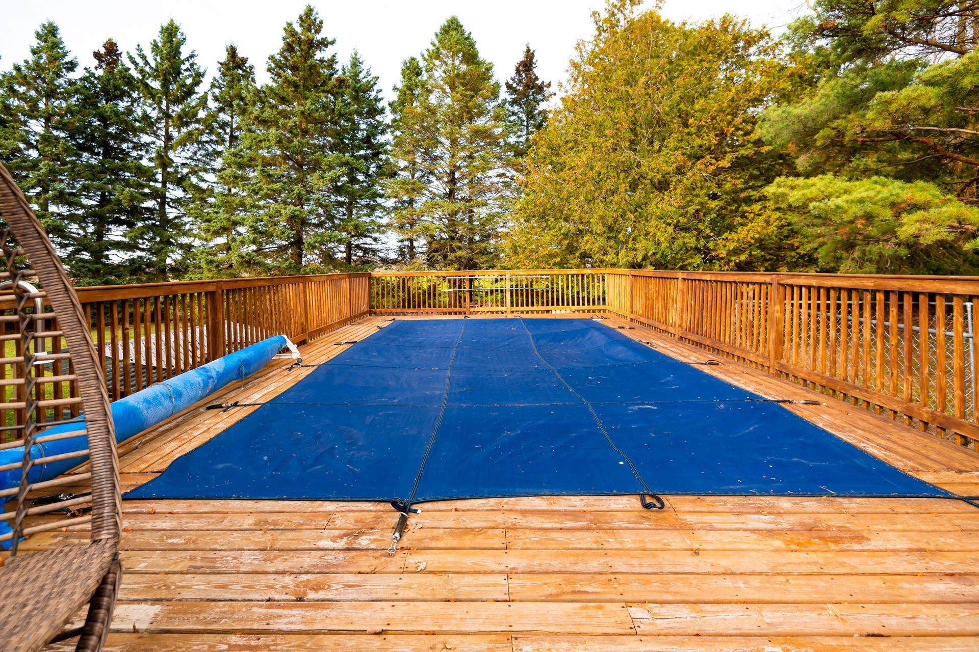 A large swimming pool is covered with a blue cover on a wooden deck.