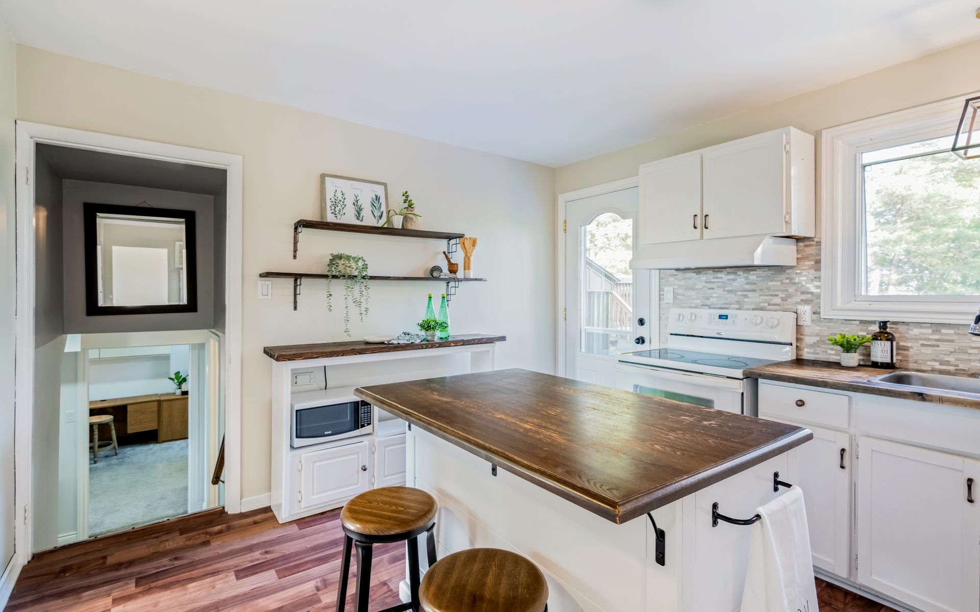 A kitchen with white cabinets , a large island , stools and a window.