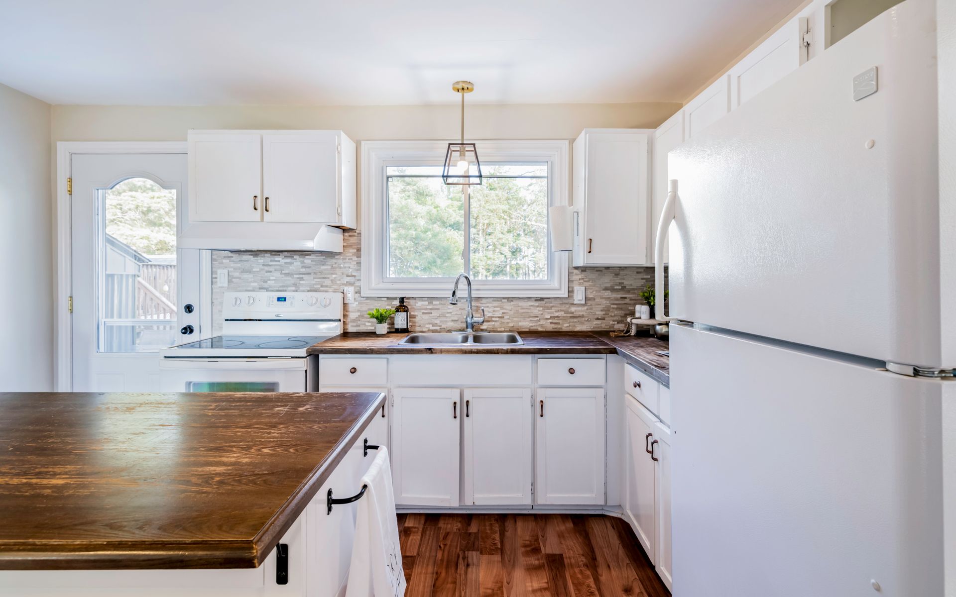 A kitchen with white cabinets , a refrigerator , a sink , and a wooden counter top.