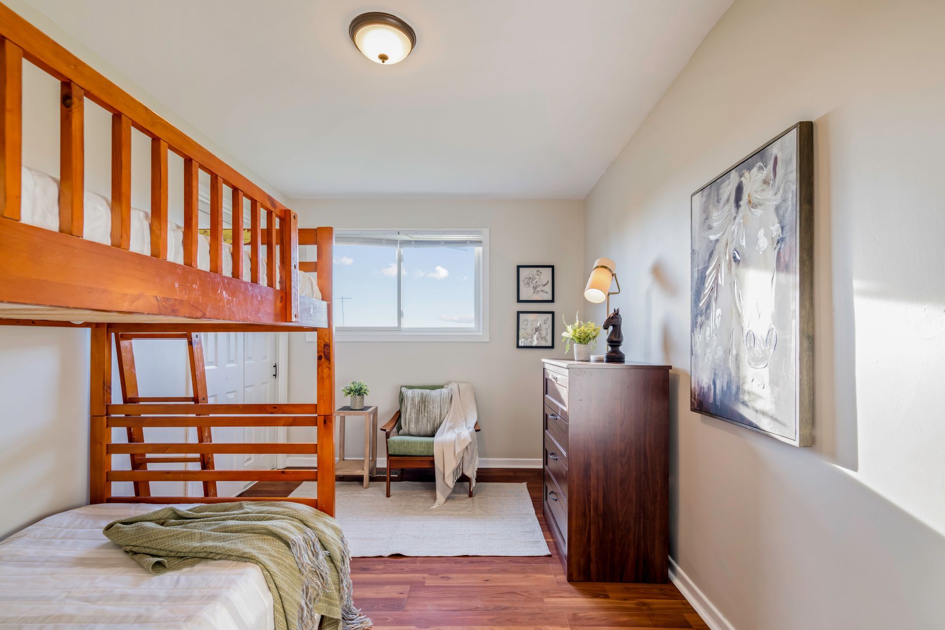 A bedroom with a bunk bed , dresser , chair and window.
