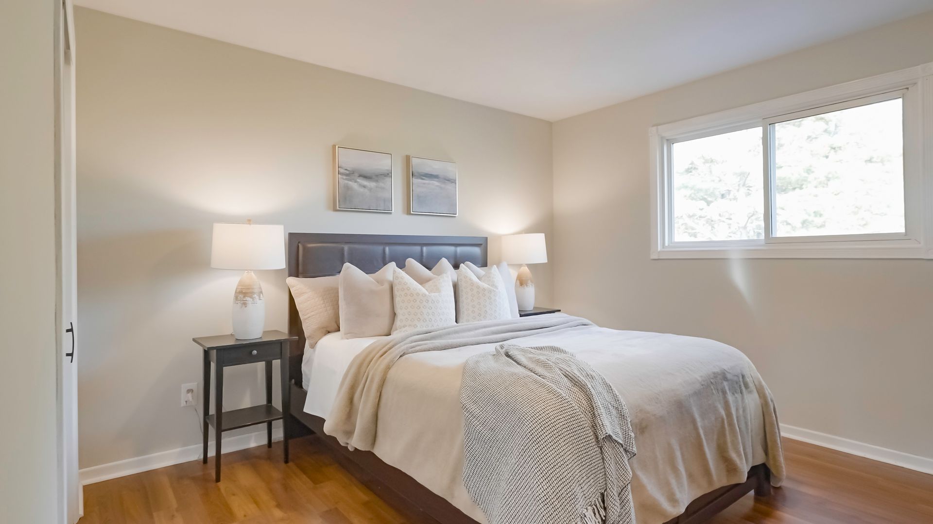 A bedroom with a bed , nightstand , lamps and a window.
