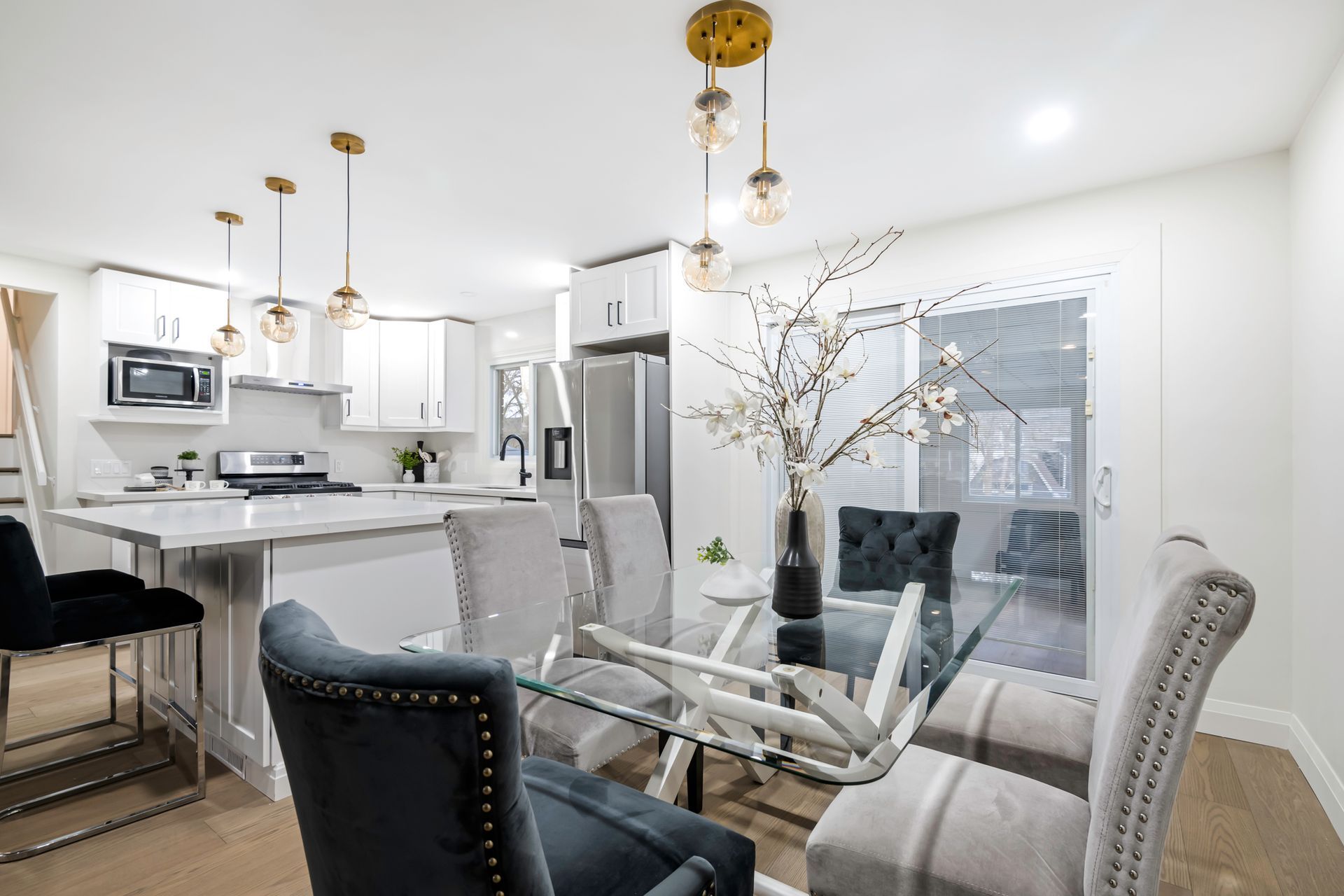 A dining room with a glass table and chairs and a kitchen in the background.