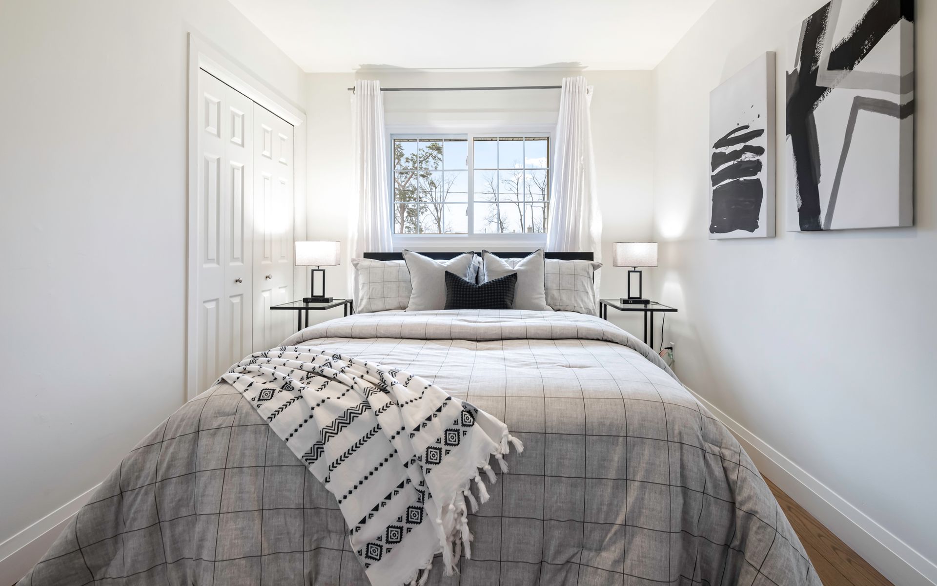 A bedroom with a bed , two nightstands , a window and two paintings on the wall.