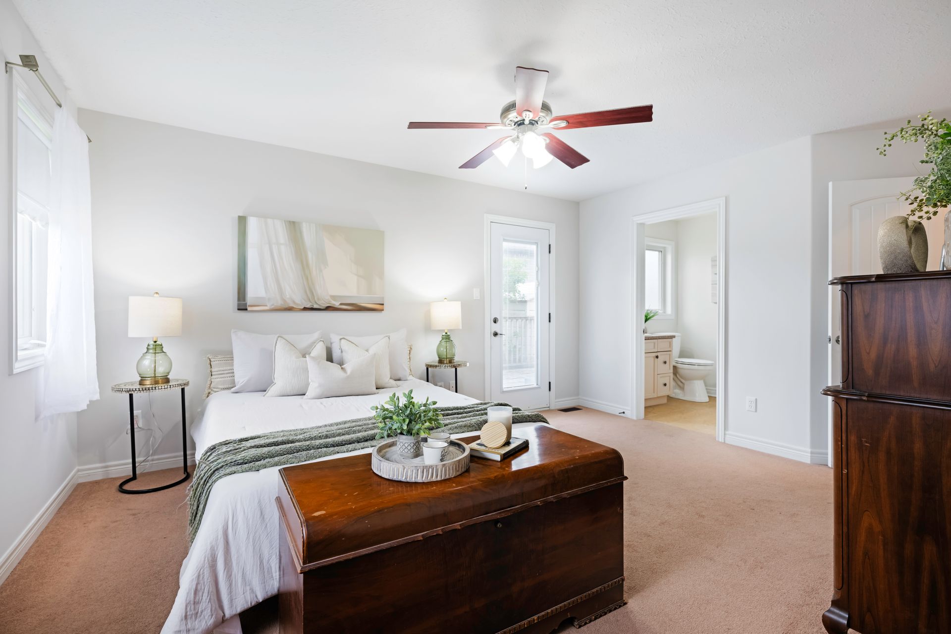 A bedroom with a bed , dresser , trunk and ceiling fan.