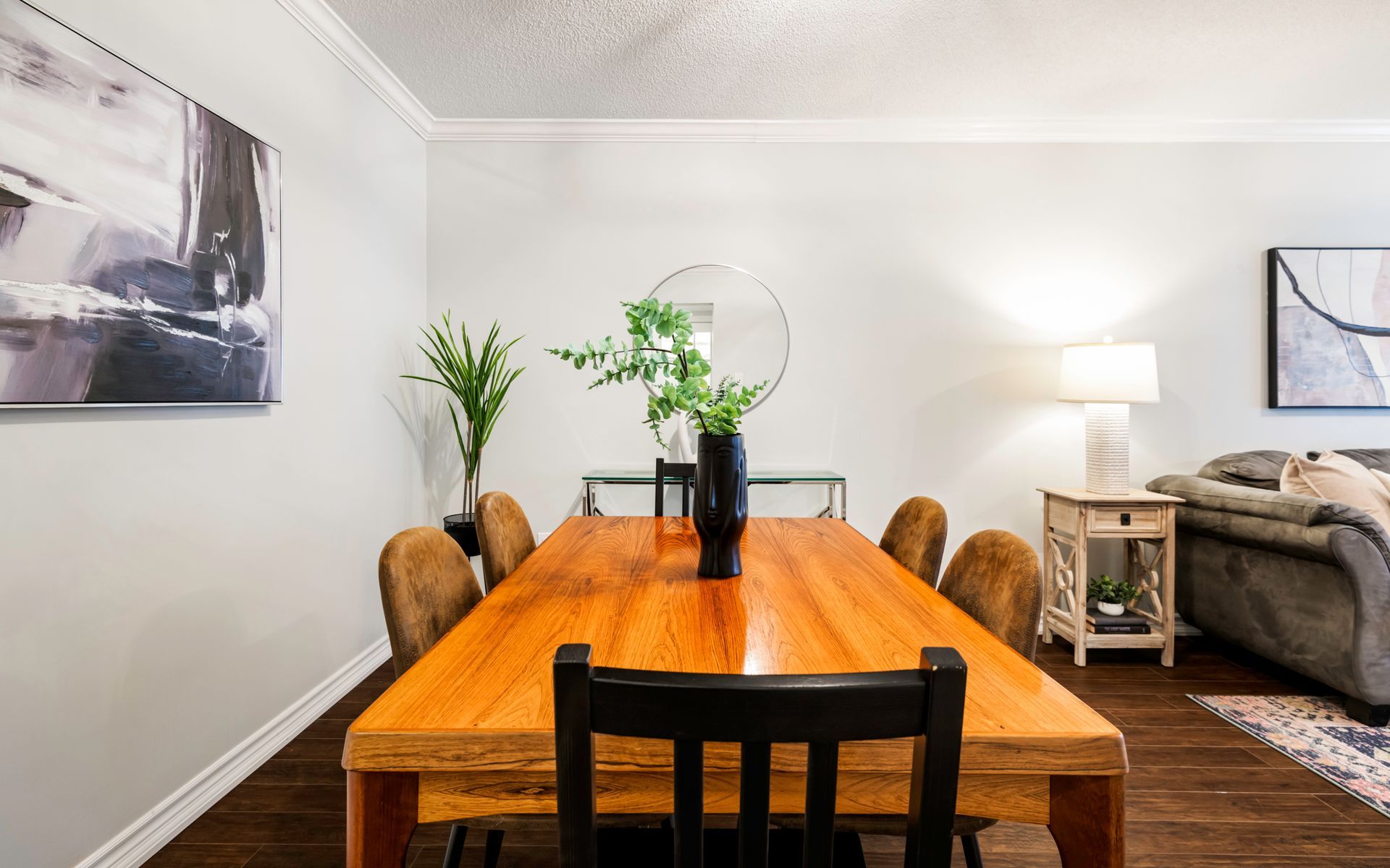 A dining room with a wooden table and chairs and a painting on the wall.