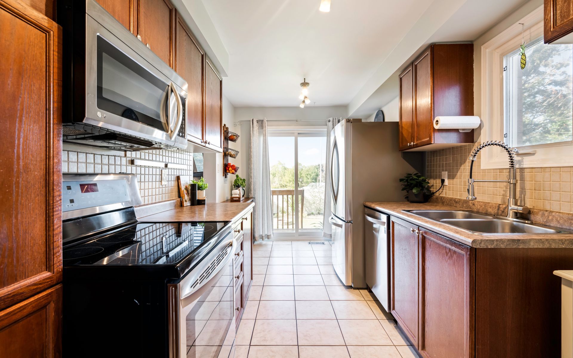 A kitchen with wooden cabinets , stainless steel appliances , a sink , stove , microwave and refrigerator