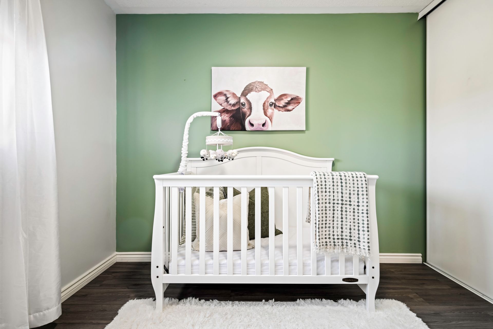 A baby 's room with a crib and a picture of cows on the wall.