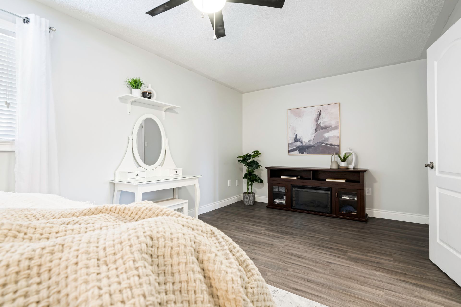 A bedroom with a bed , vanity , television and ceiling fan.