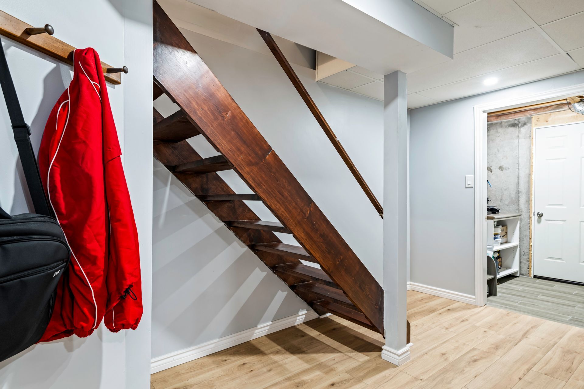 A wooden staircase in a basement with a red jacket hanging on a hook.