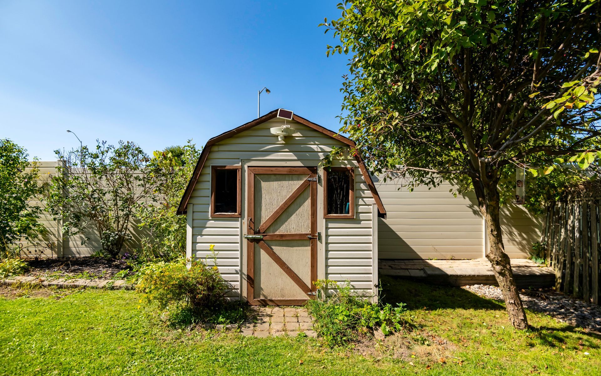A white barn shed is sitting in the middle of a lush green yard.