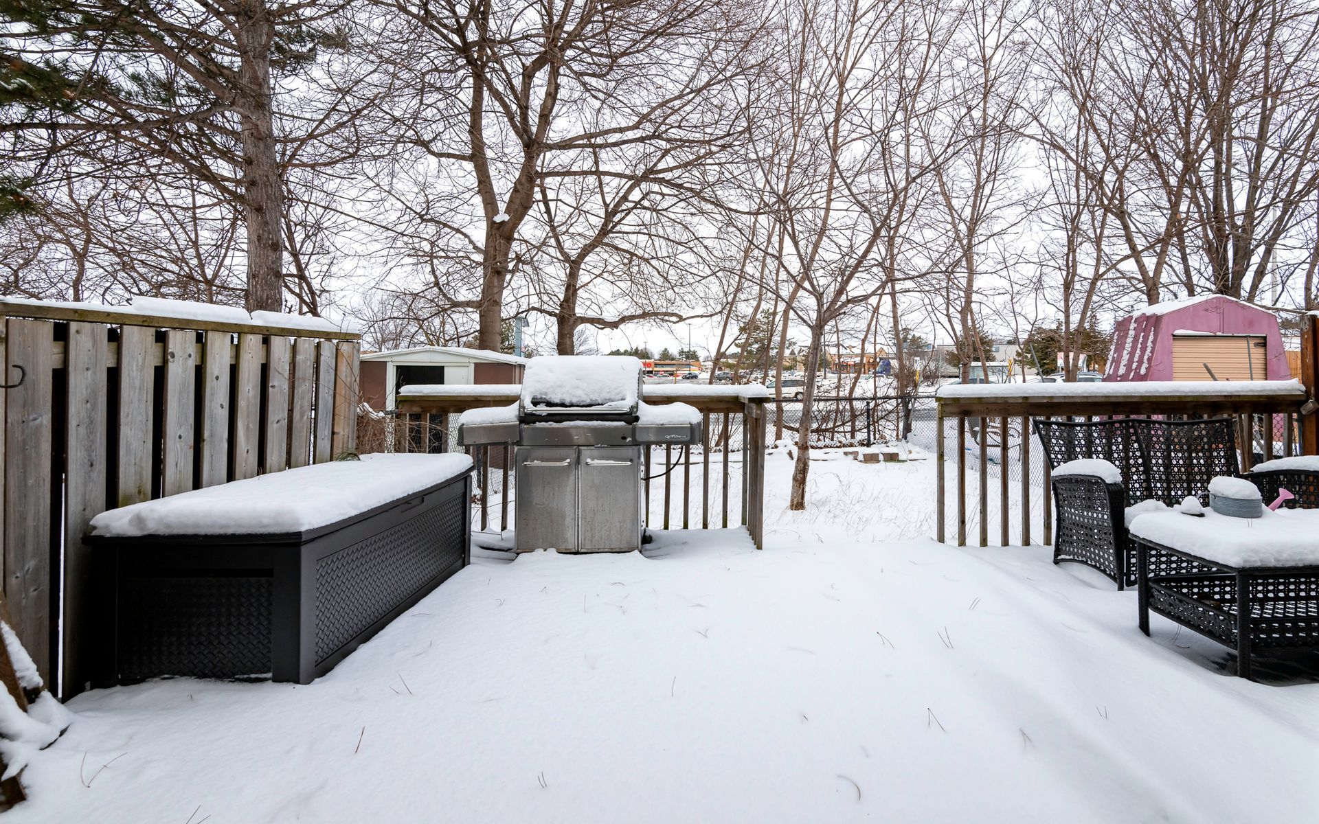 A backyard covered in snow with a grill and a bench.