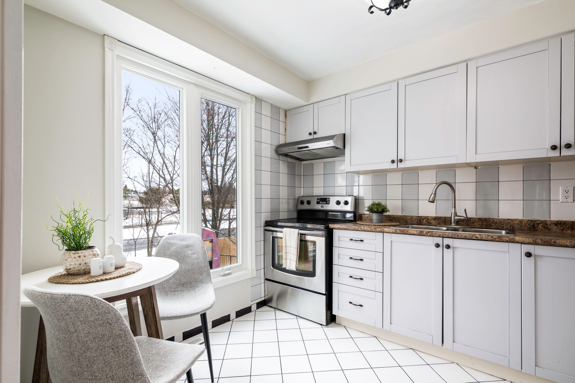 A kitchen with white cabinets , a stove , a table and chairs.