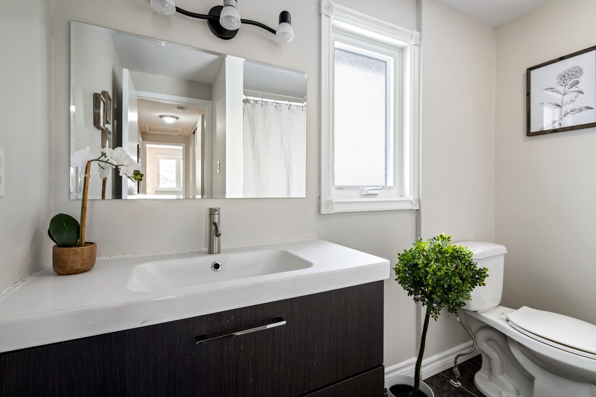 A bathroom with a sink , toilet , mirror and window.