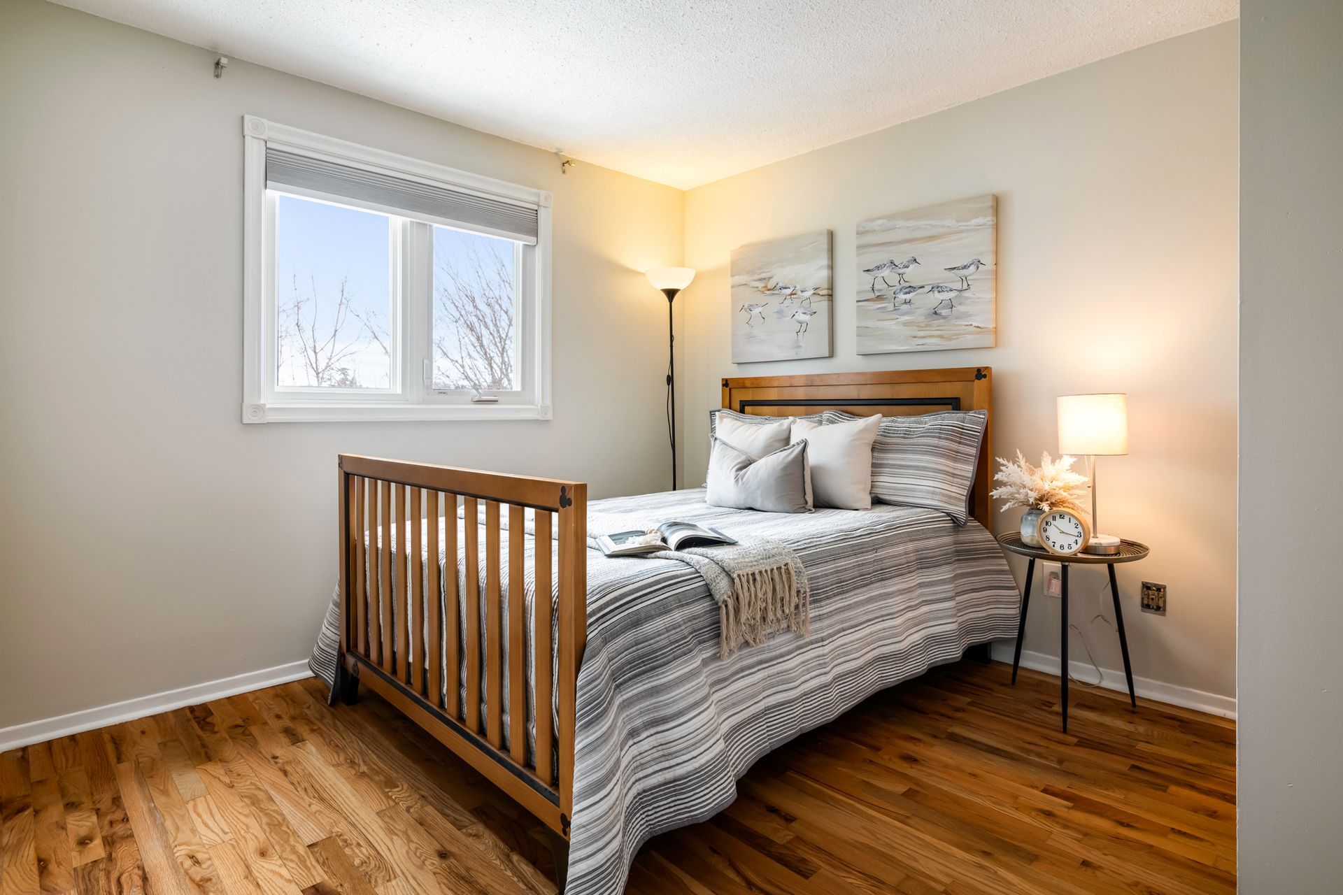 A bedroom with a bed , nightstand , lamp and window.