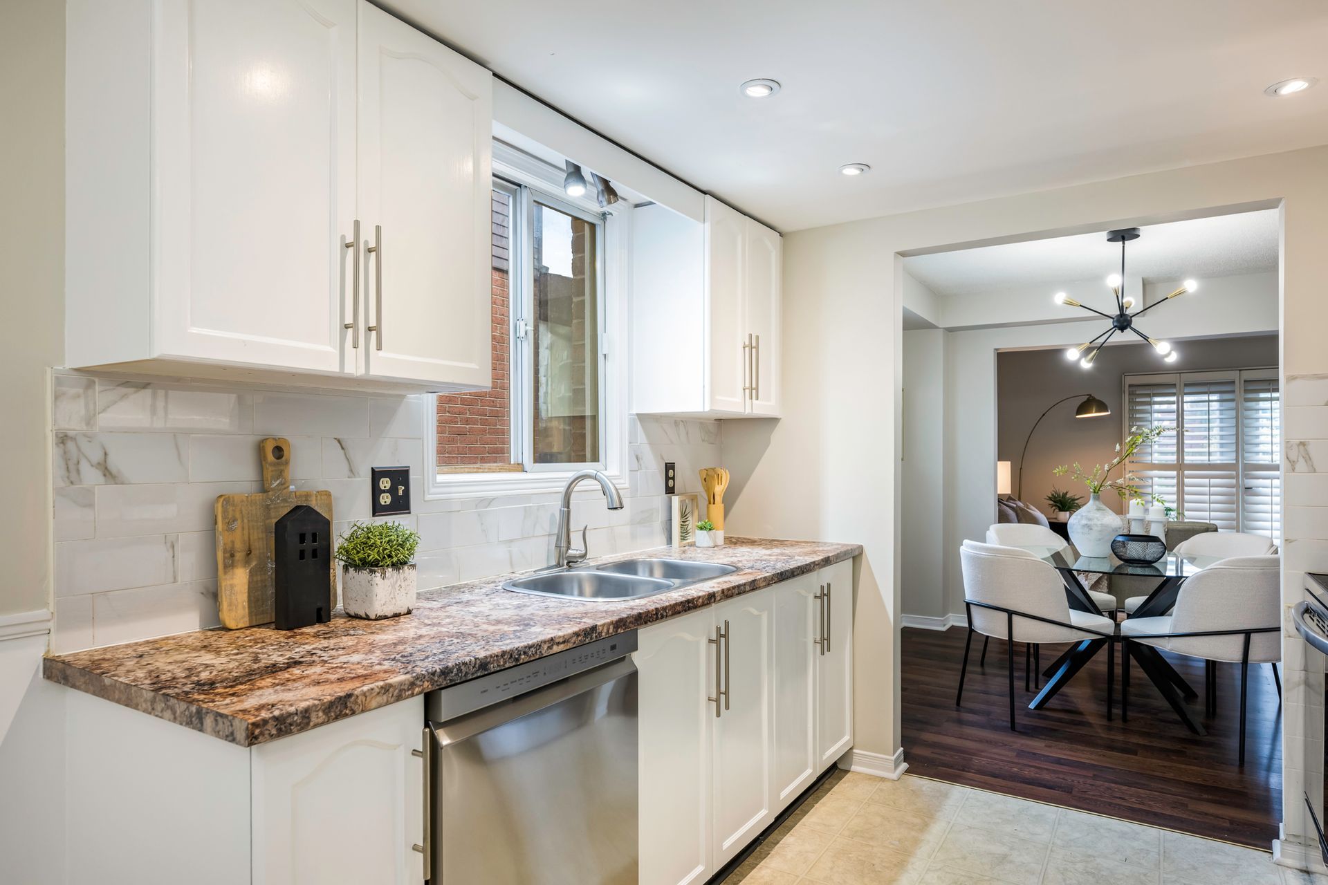 A kitchen with white cabinets , granite counter tops , a sink and a dishwasher.