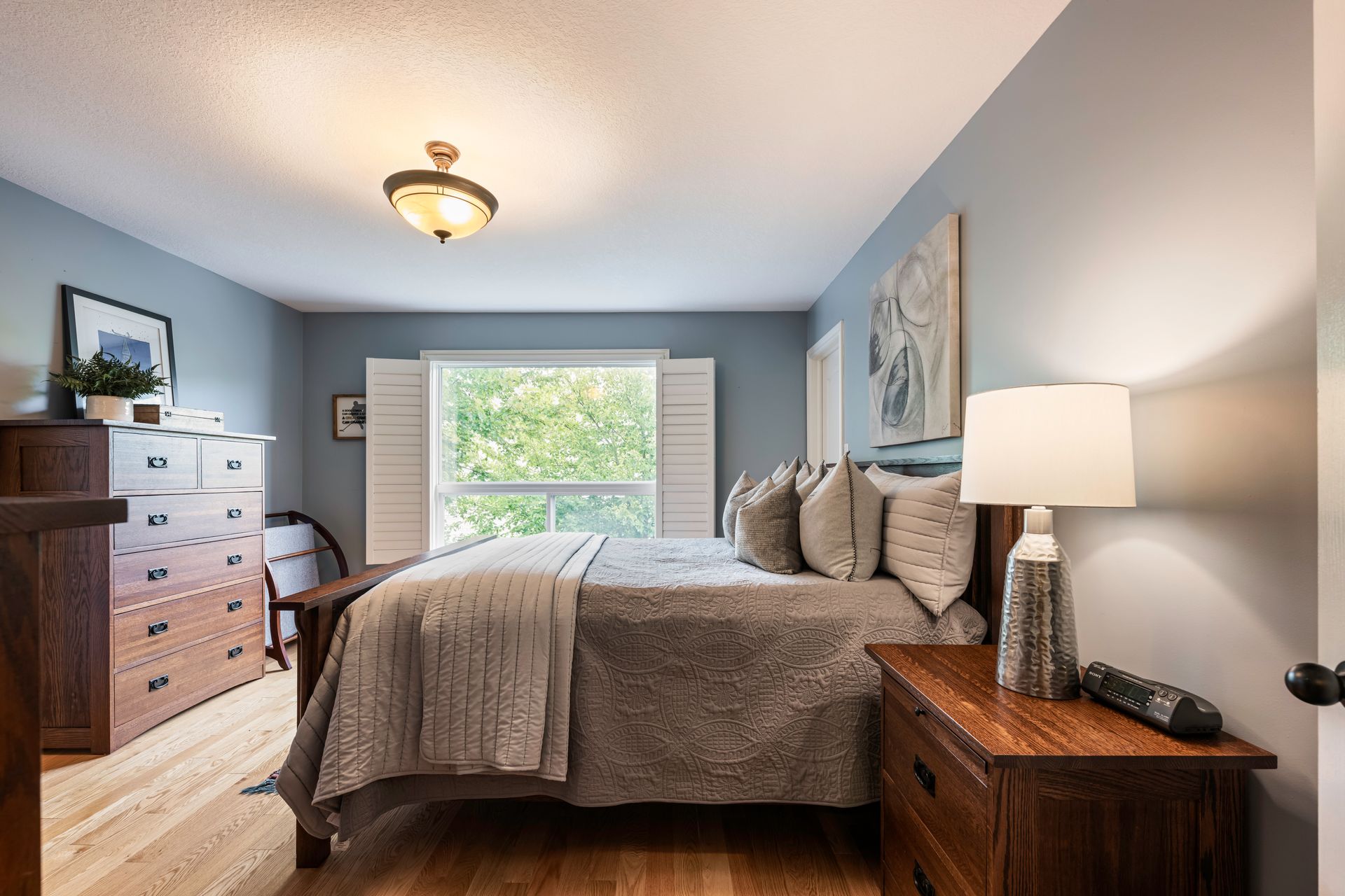 A bedroom with a bed , nightstand , dresser and window.