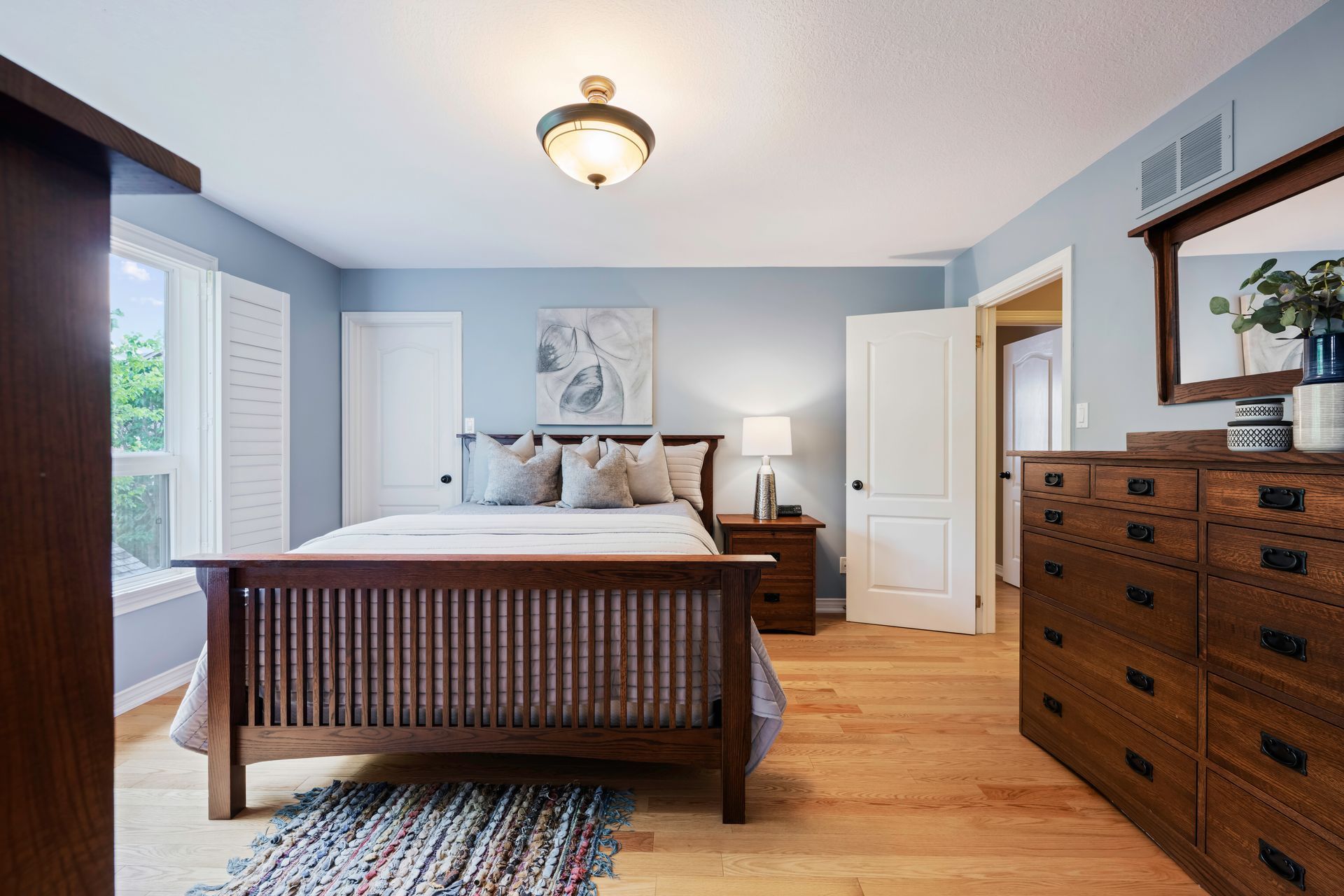 A bedroom with a bed , dresser , mirror and window.