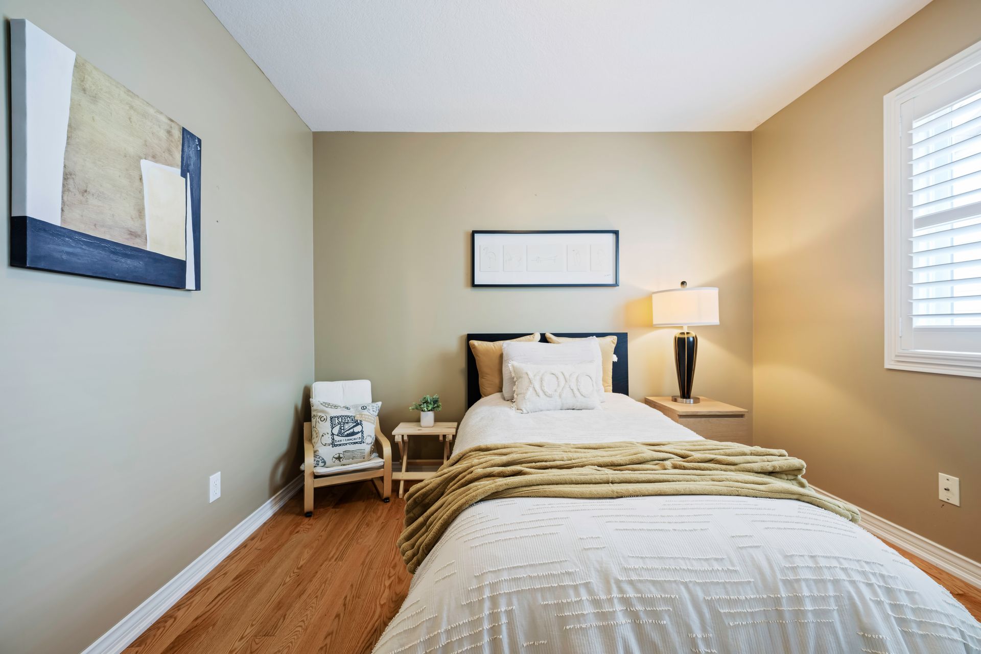 A bedroom with a bed , chair , lamp and painting on the wall.