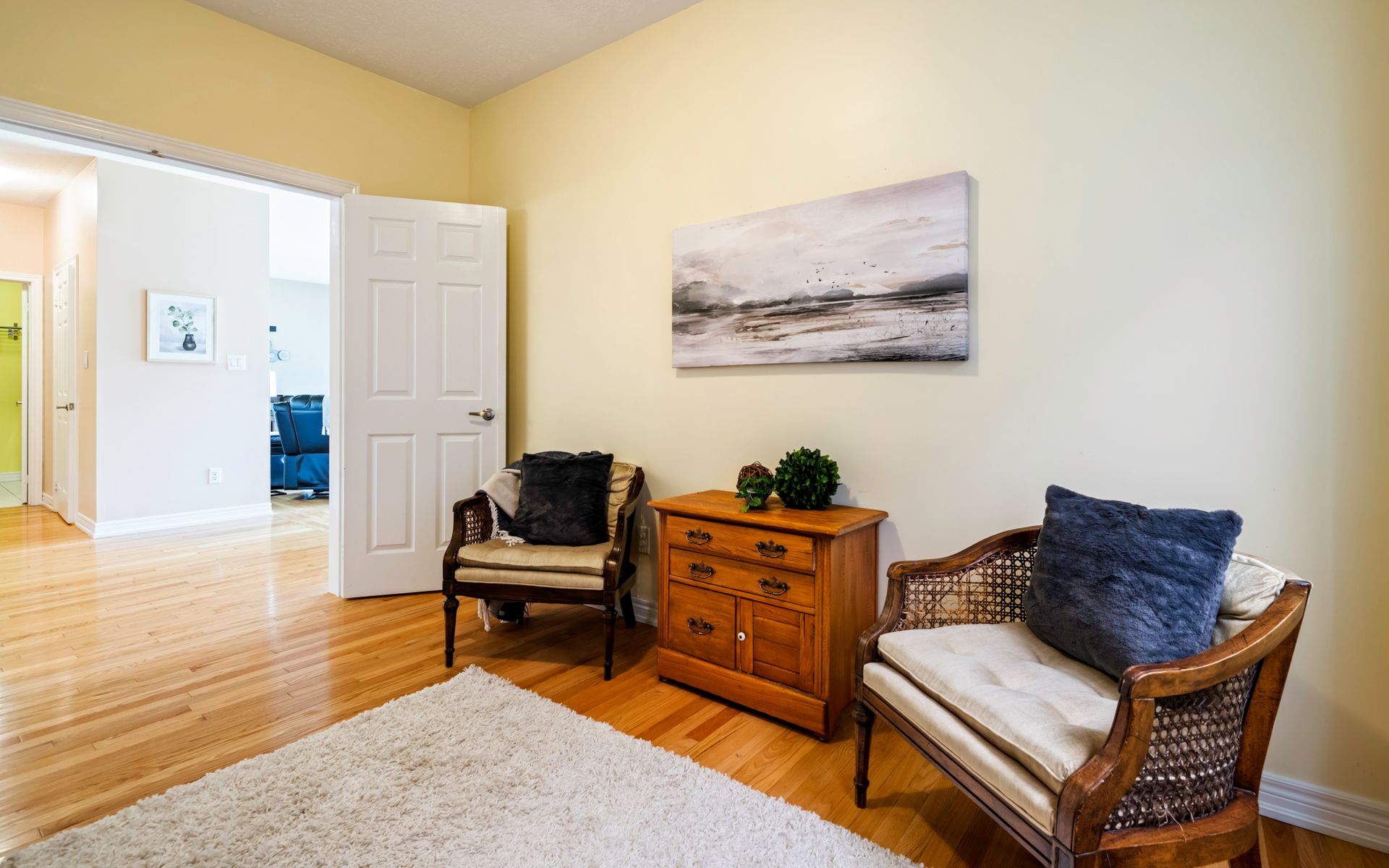 A living room with two chairs , a dresser and a painting on the wall.