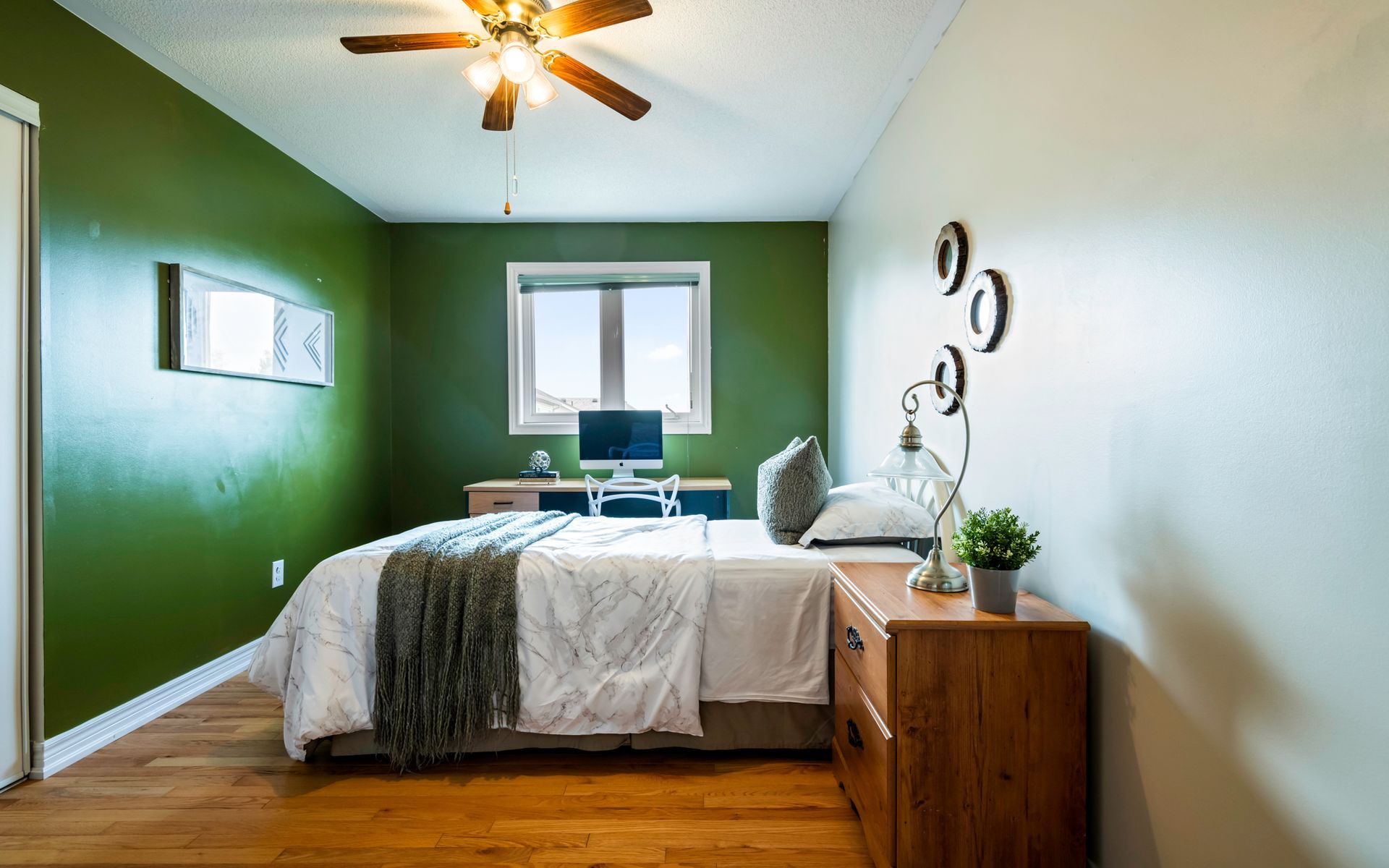 A bedroom with green walls , a bed , a desk and a ceiling fan.