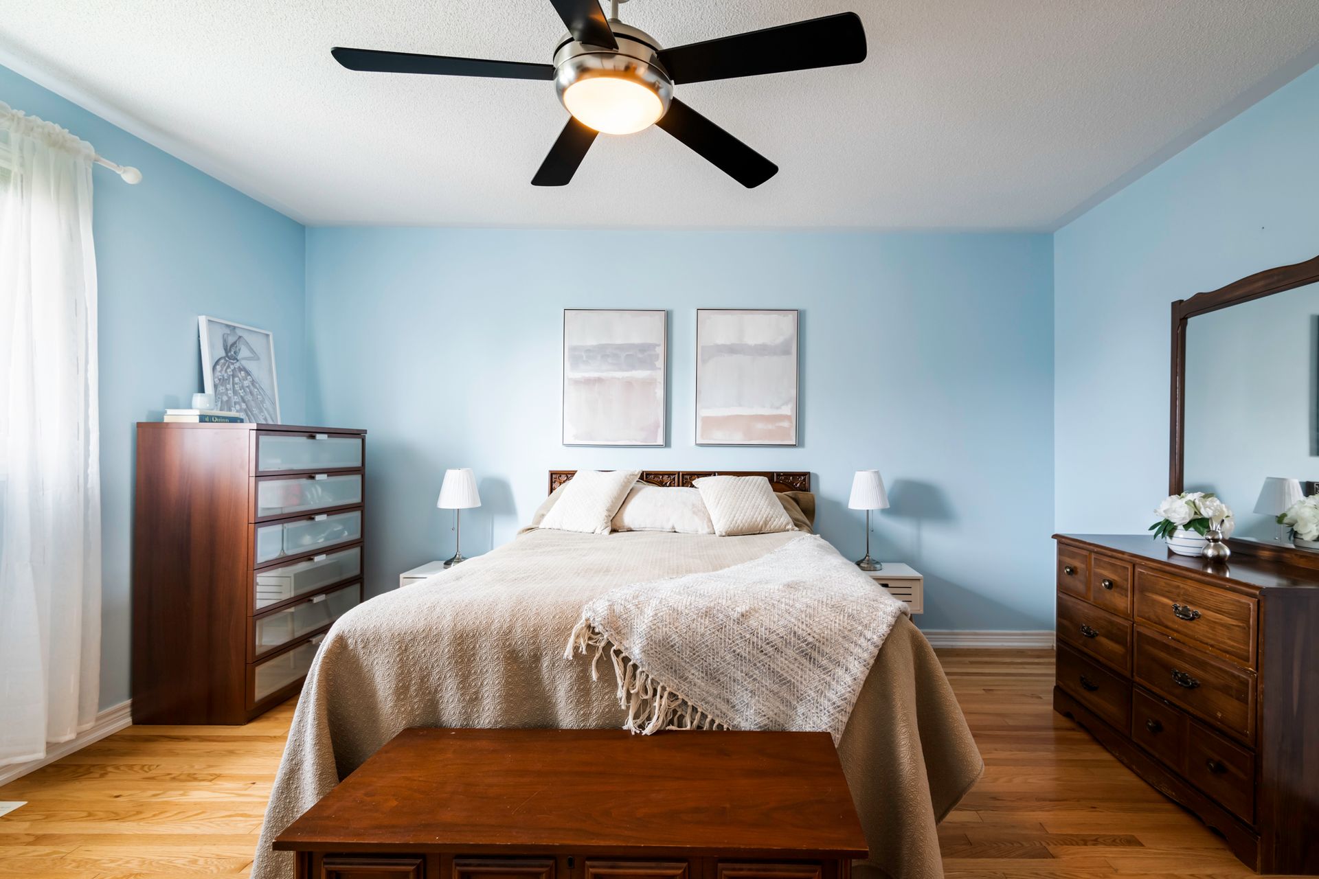 A bedroom with a bed , dresser , mirror and ceiling fan.
