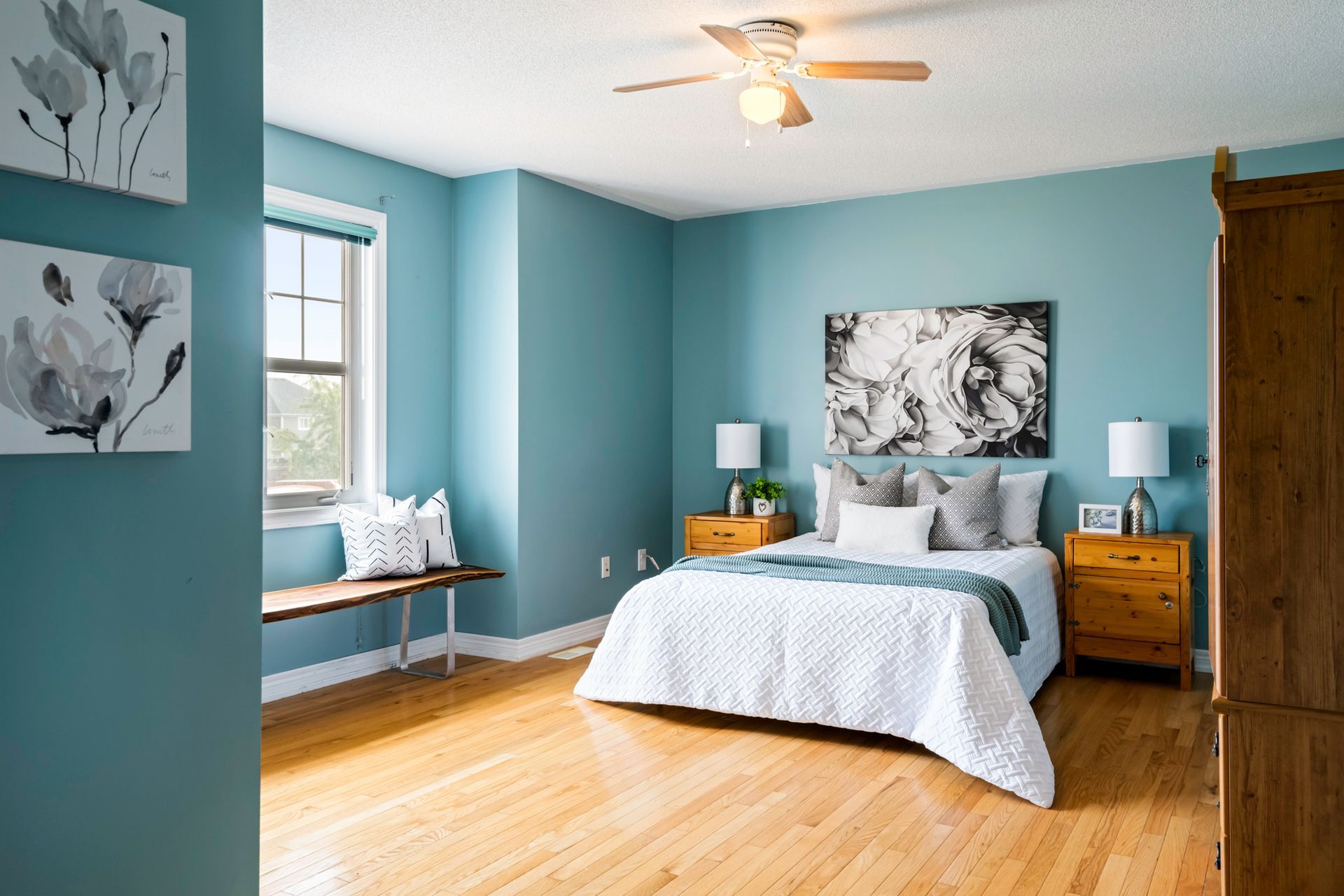 A bedroom with blue walls , a bed , nightstands , a bench and a ceiling fan.