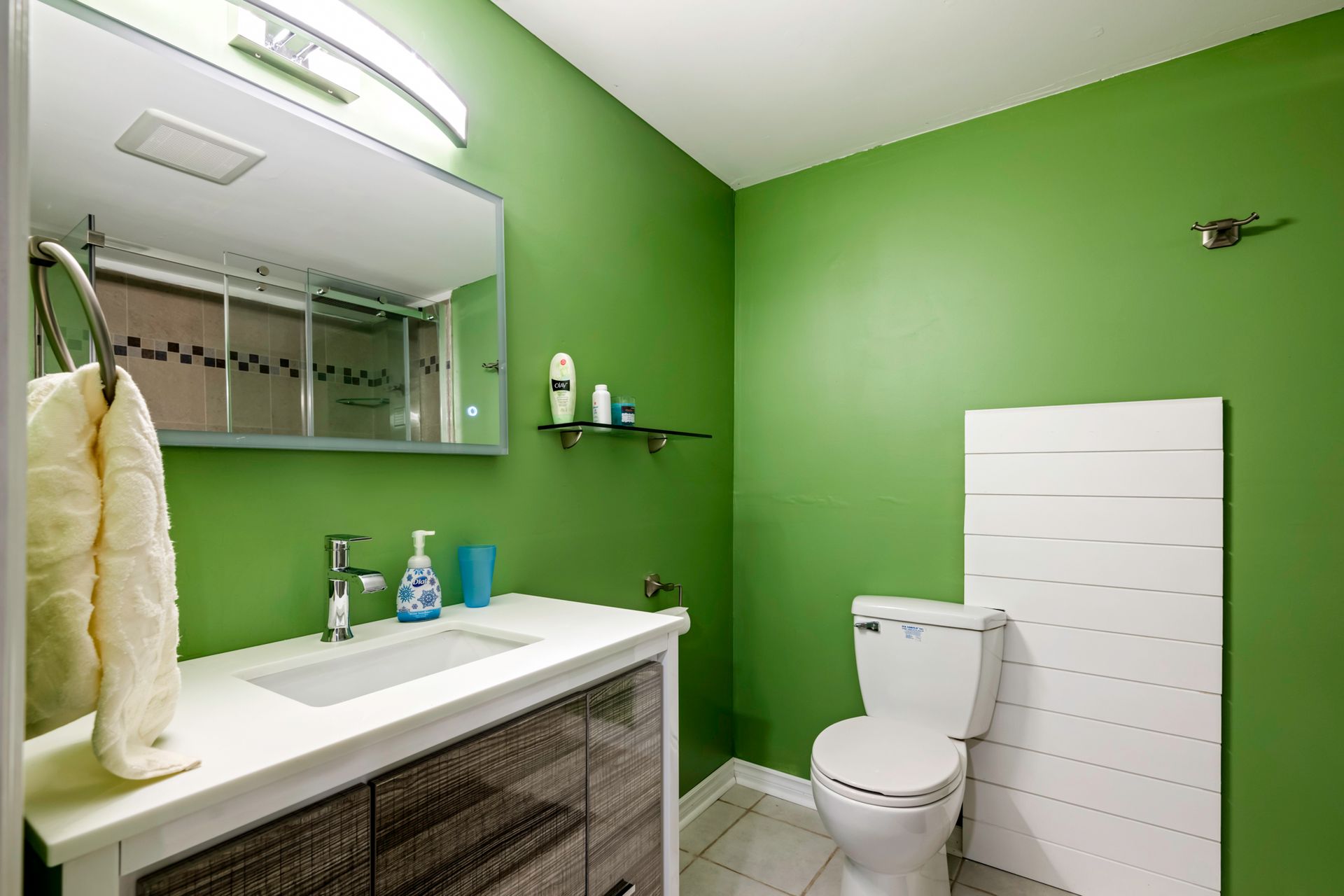A bathroom with green walls , a sink , toilet and mirror.