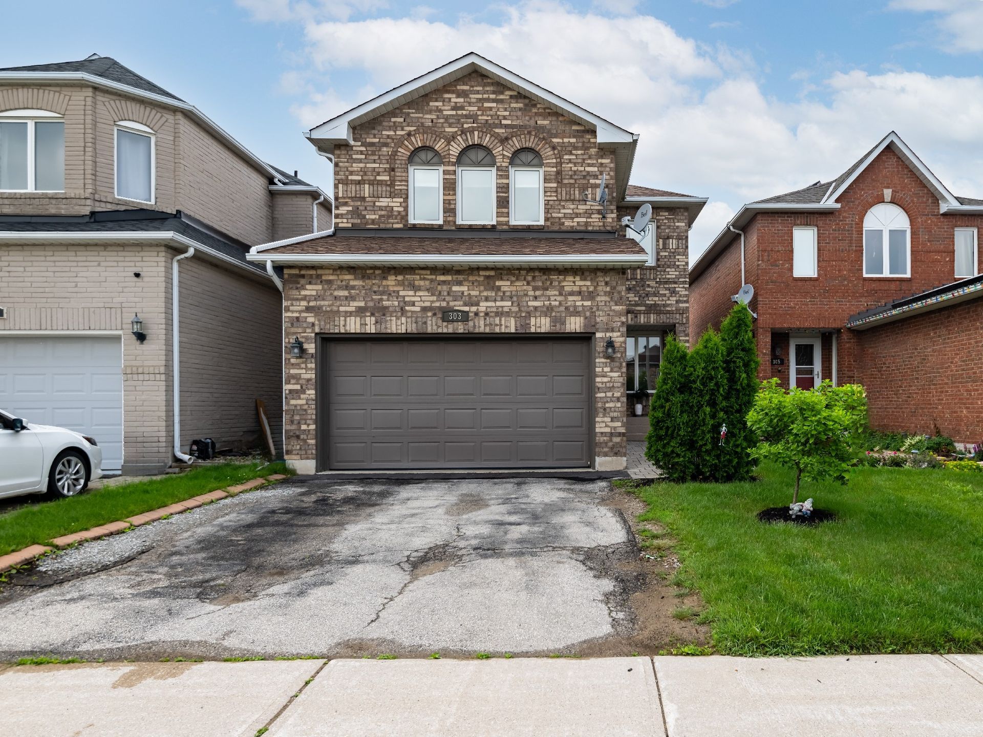 A white car is parked in front of a large brick house.