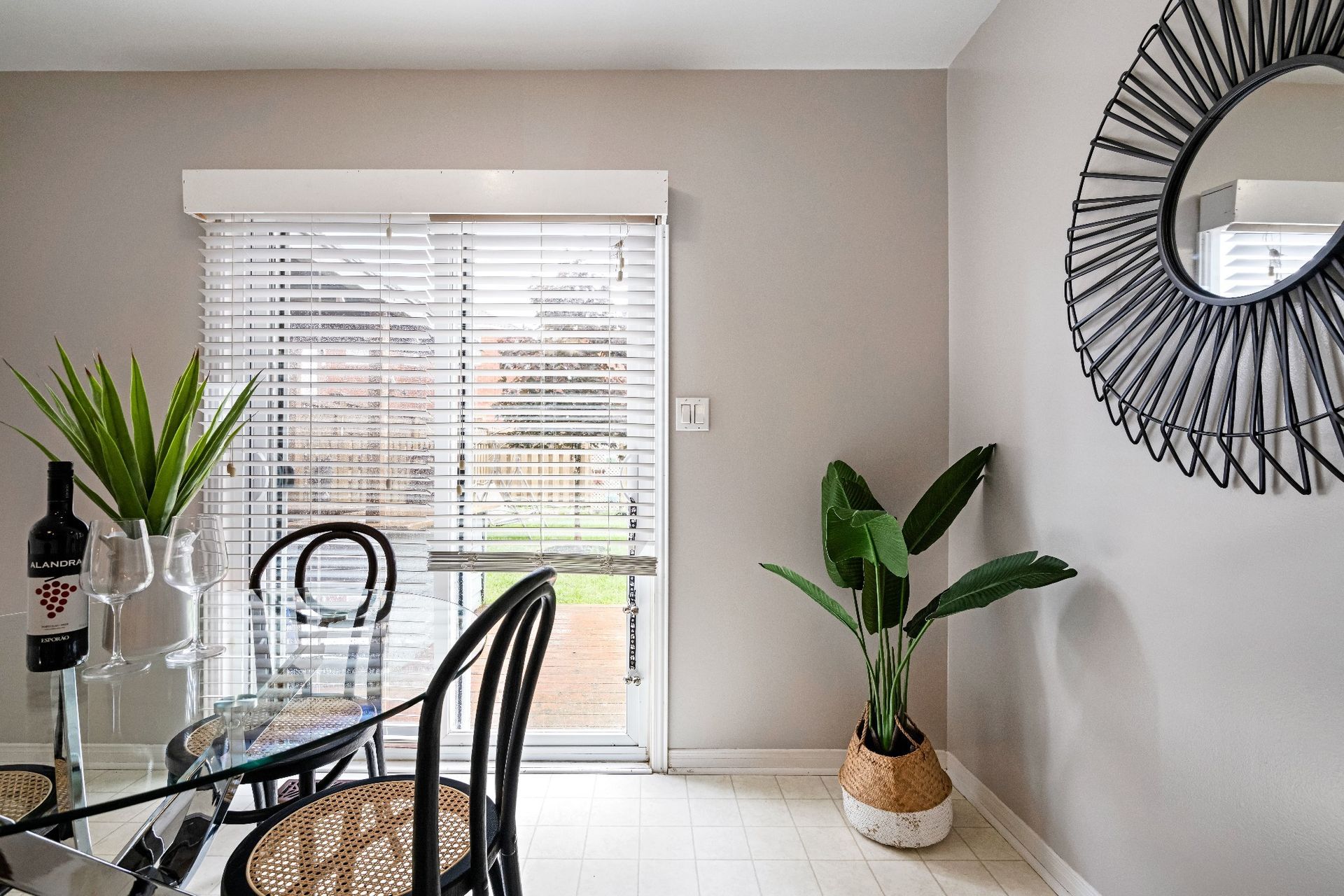 A dining room with a table , chairs , a plant and a mirror.