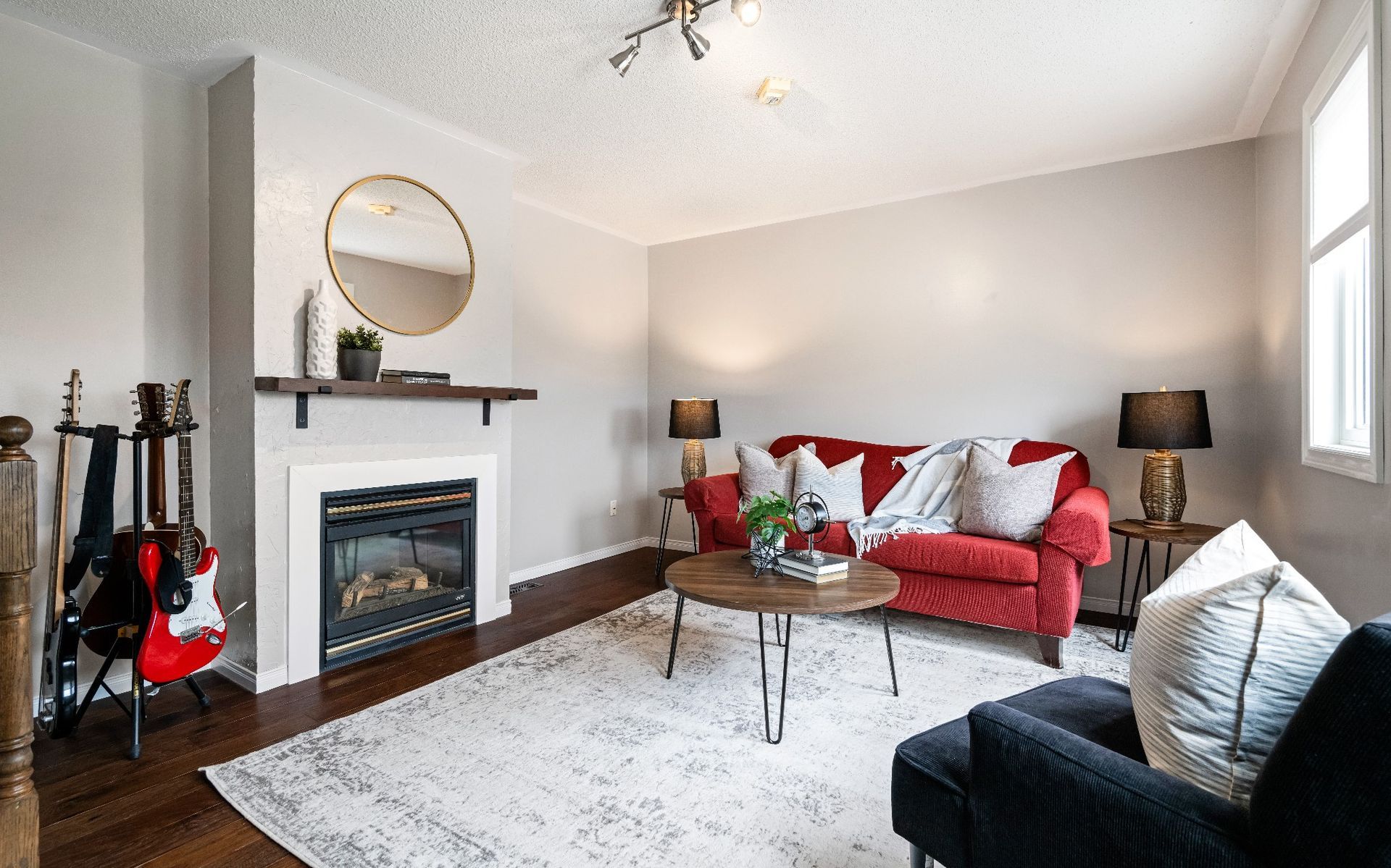 A living room with a red couch , black chair , coffee table and fireplace.