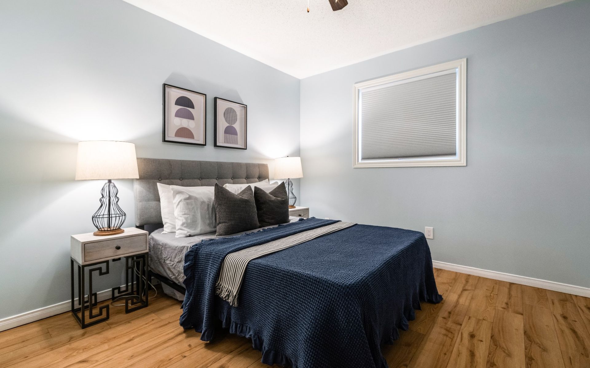 A bedroom with a bed , nightstand , lamps and a ceiling fan.
