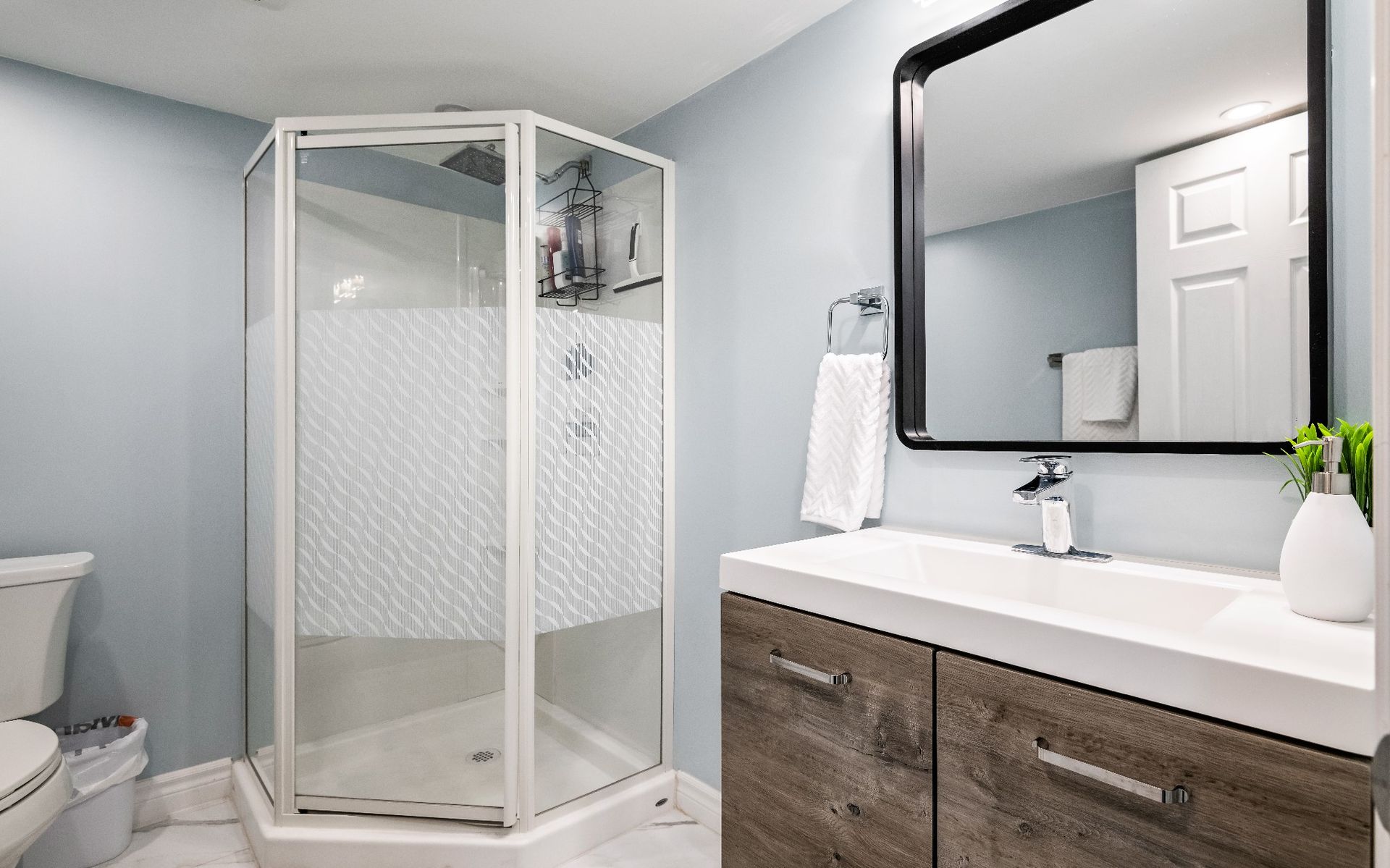 A bathroom with a shower , sink , toilet and mirror.