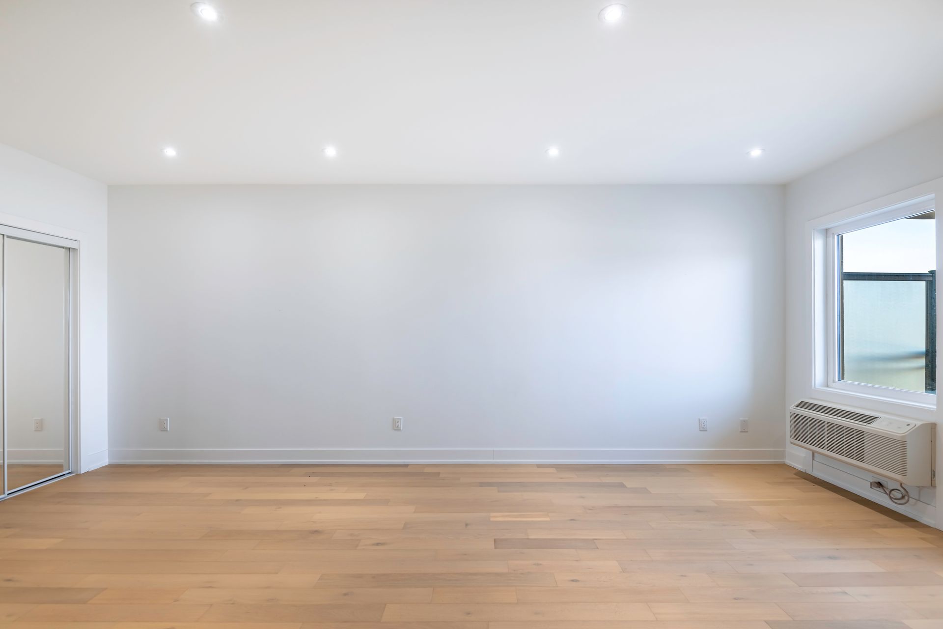An empty living room with hardwood floors and white walls.