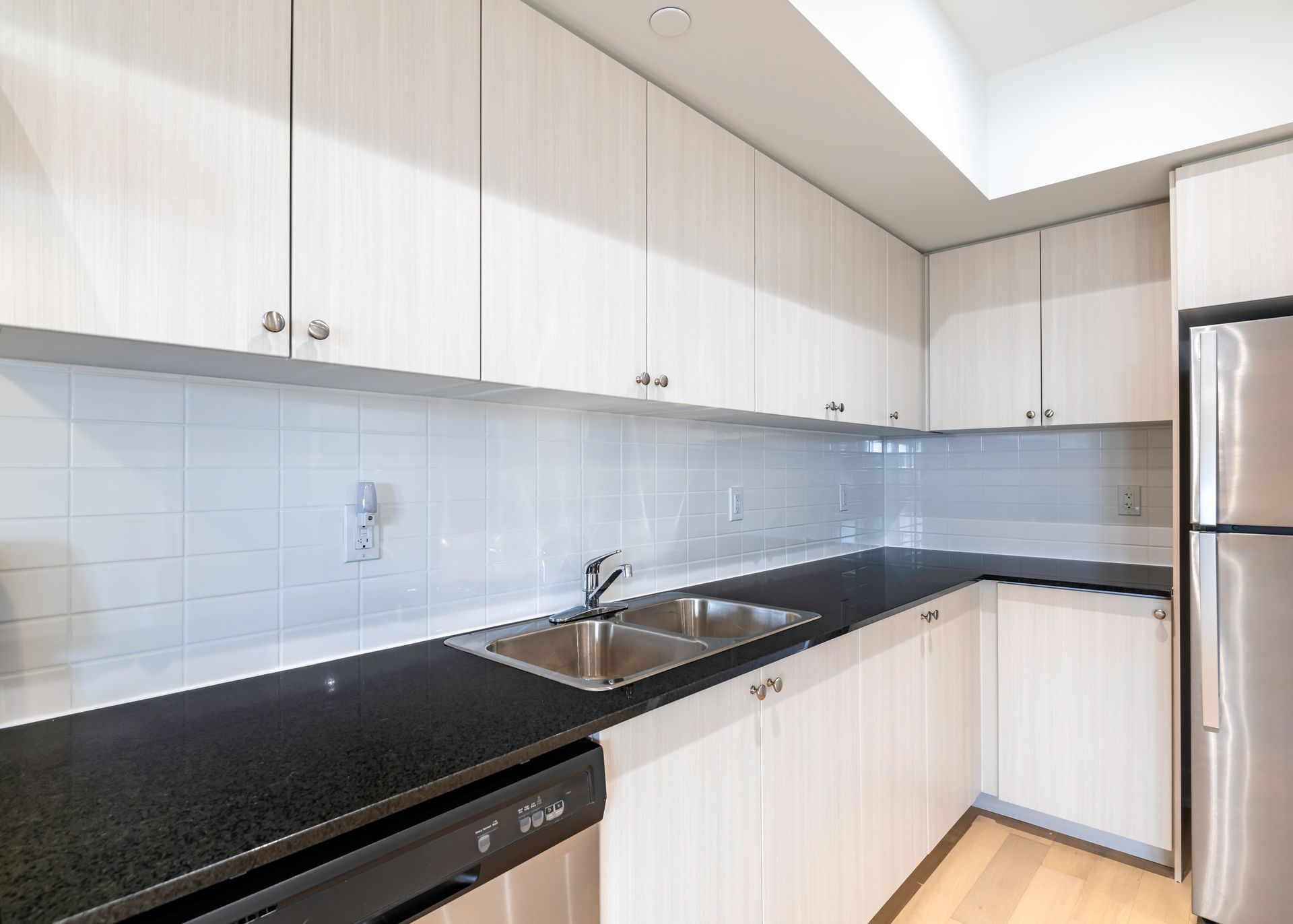 A kitchen with white cabinets , black counter tops , stainless steel appliances and a refrigerator.