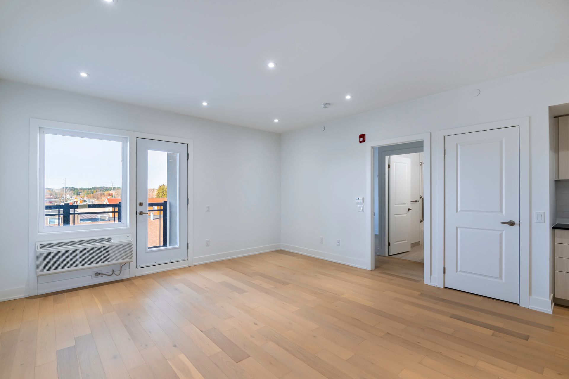 An empty living room with hardwood floors and a balcony.