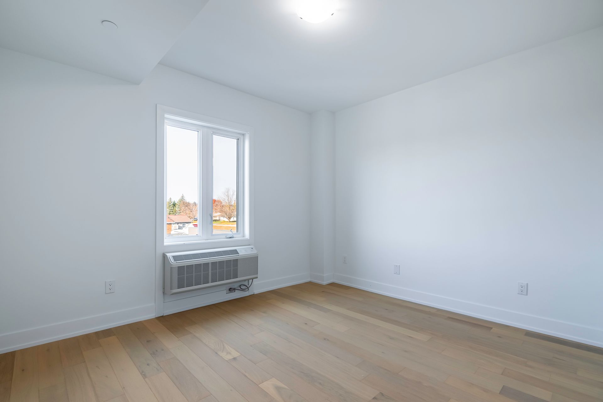 An empty room with hardwood floors , white walls and a window.