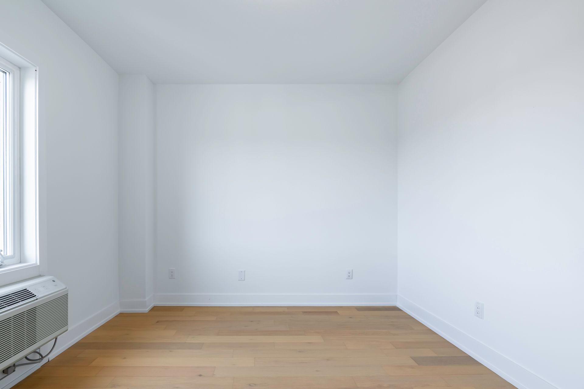 an empty room with hardwood floors , white walls and a window .