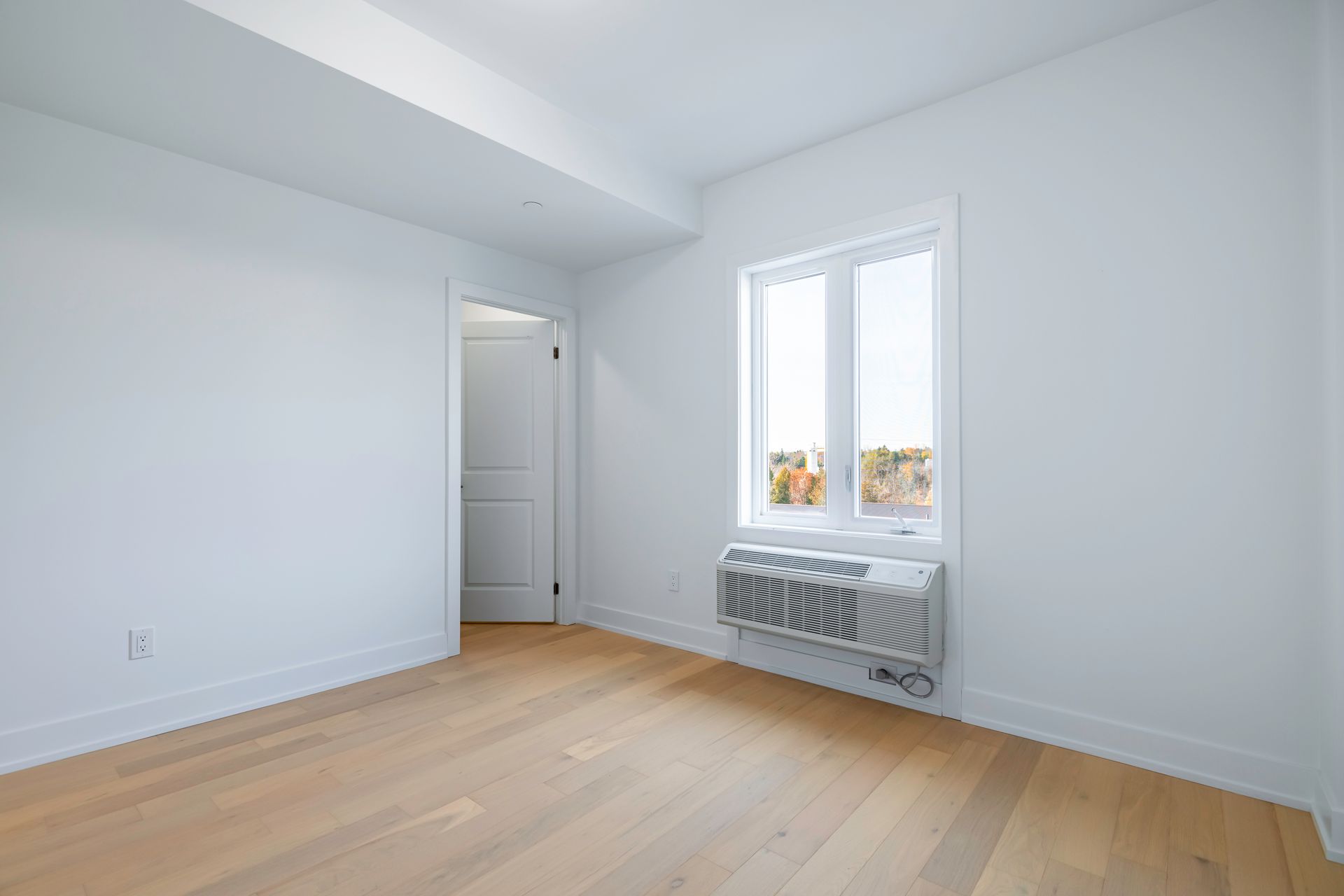 An empty room with hardwood floors , white walls and a window.