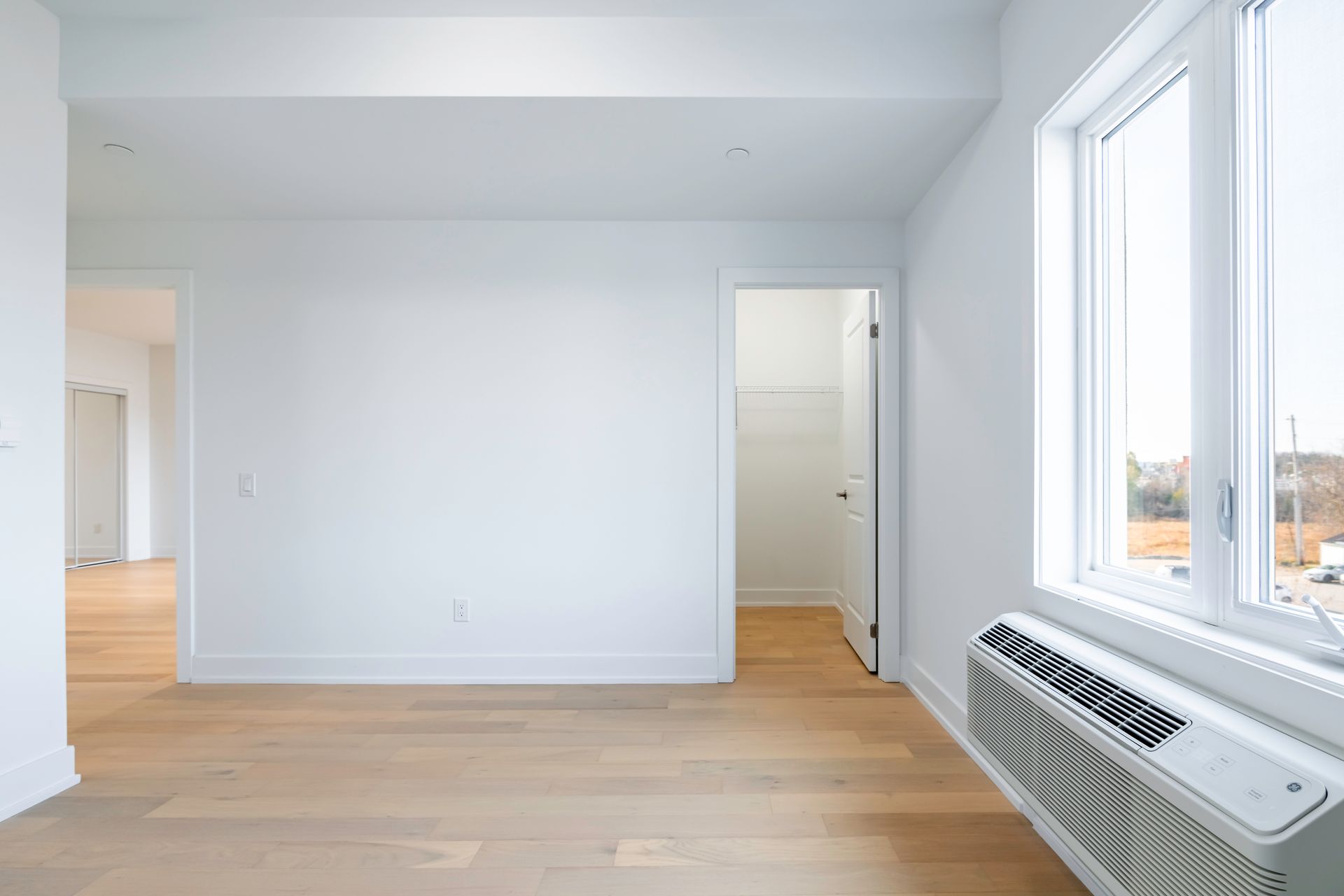 An empty room with hardwood floors , white walls and a window.