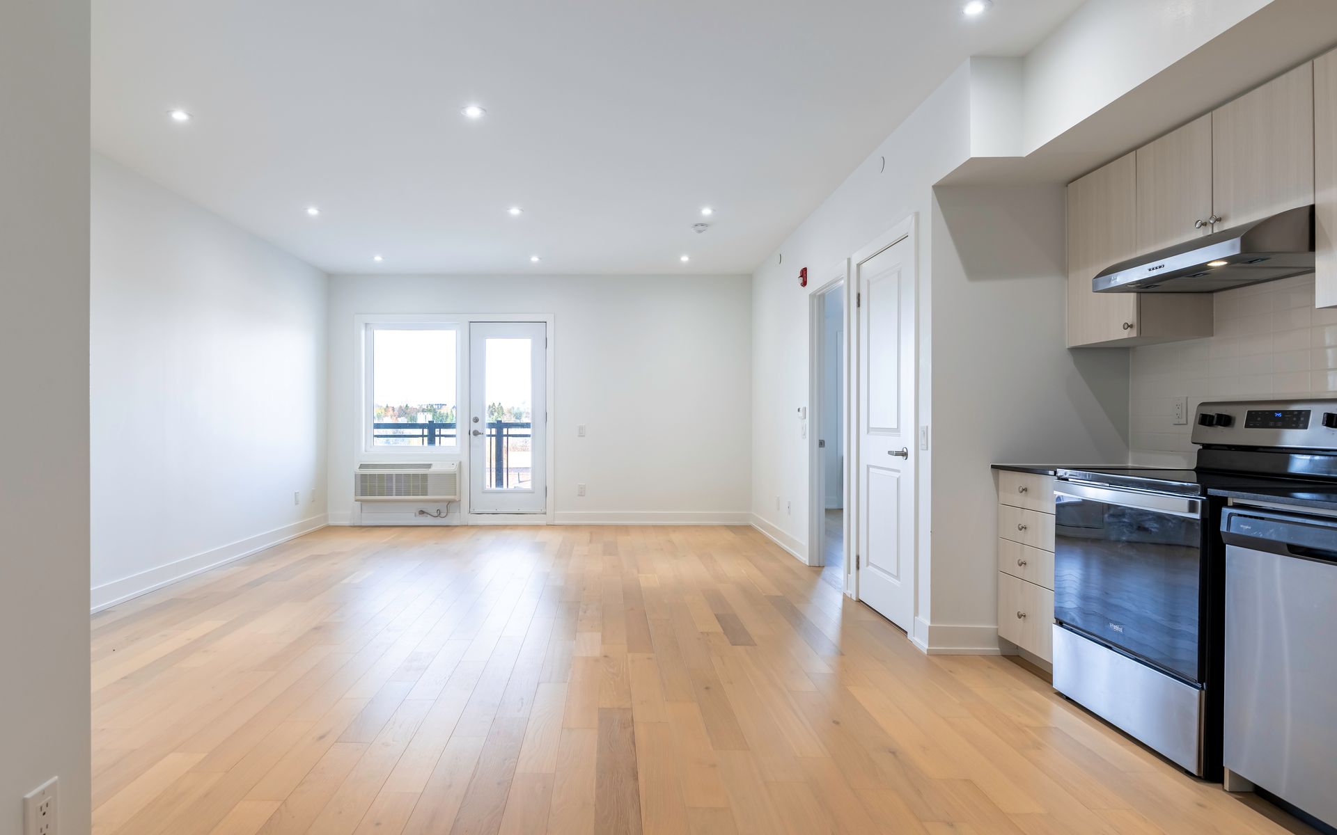An empty apartment with hardwood floors and a kitchen.