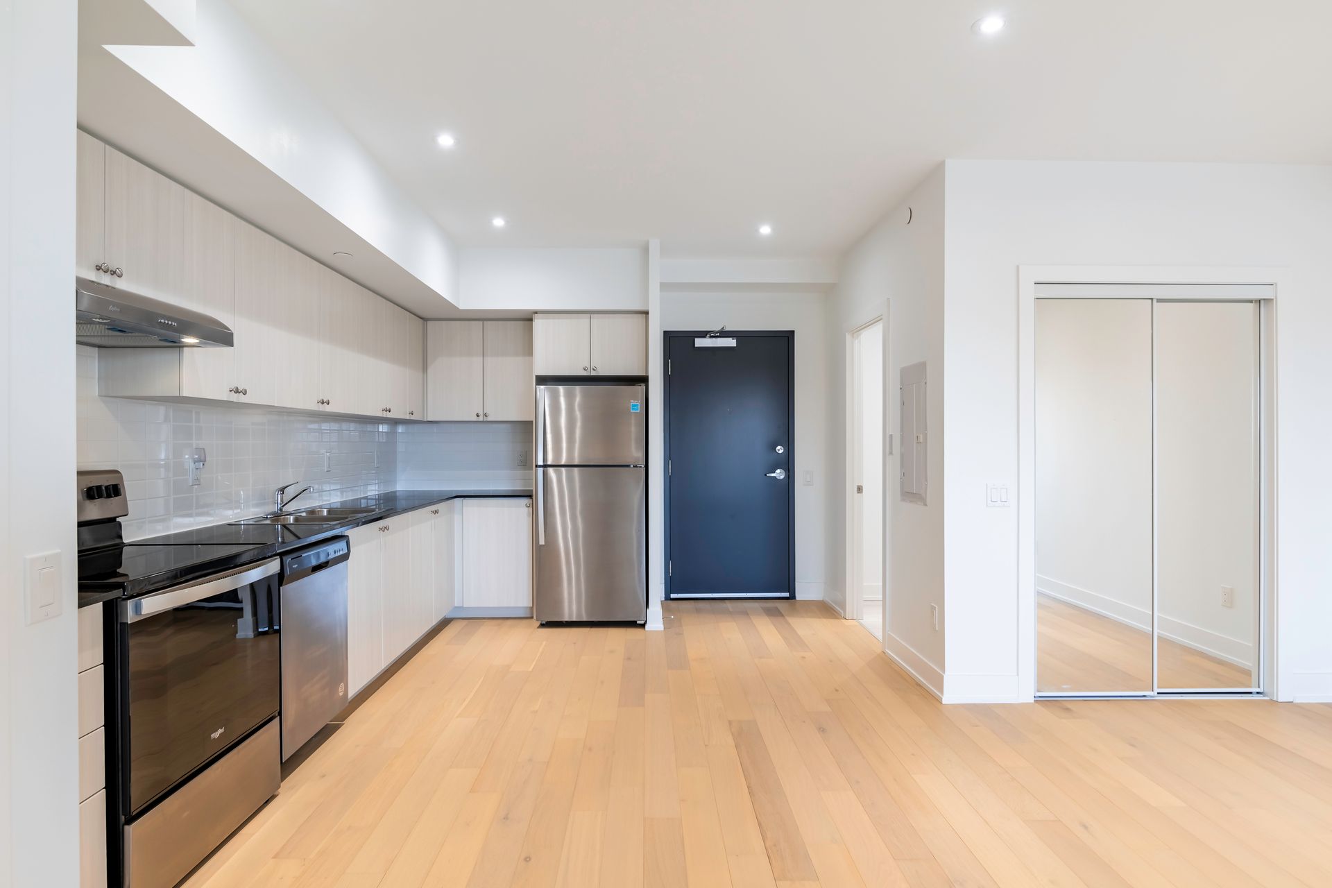 a kitchen with stainless steel appliances and hardwood floors in an empty apartment .