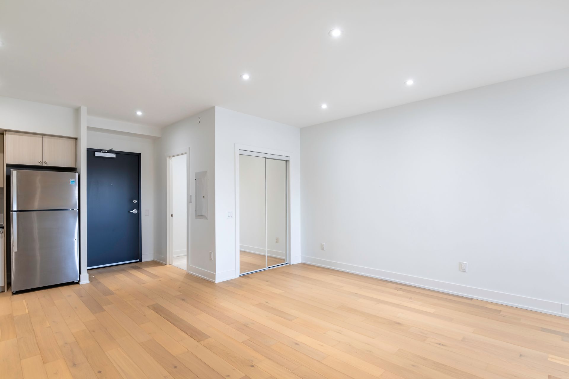 An empty living room with hardwood floors and a stainless steel refrigerator.