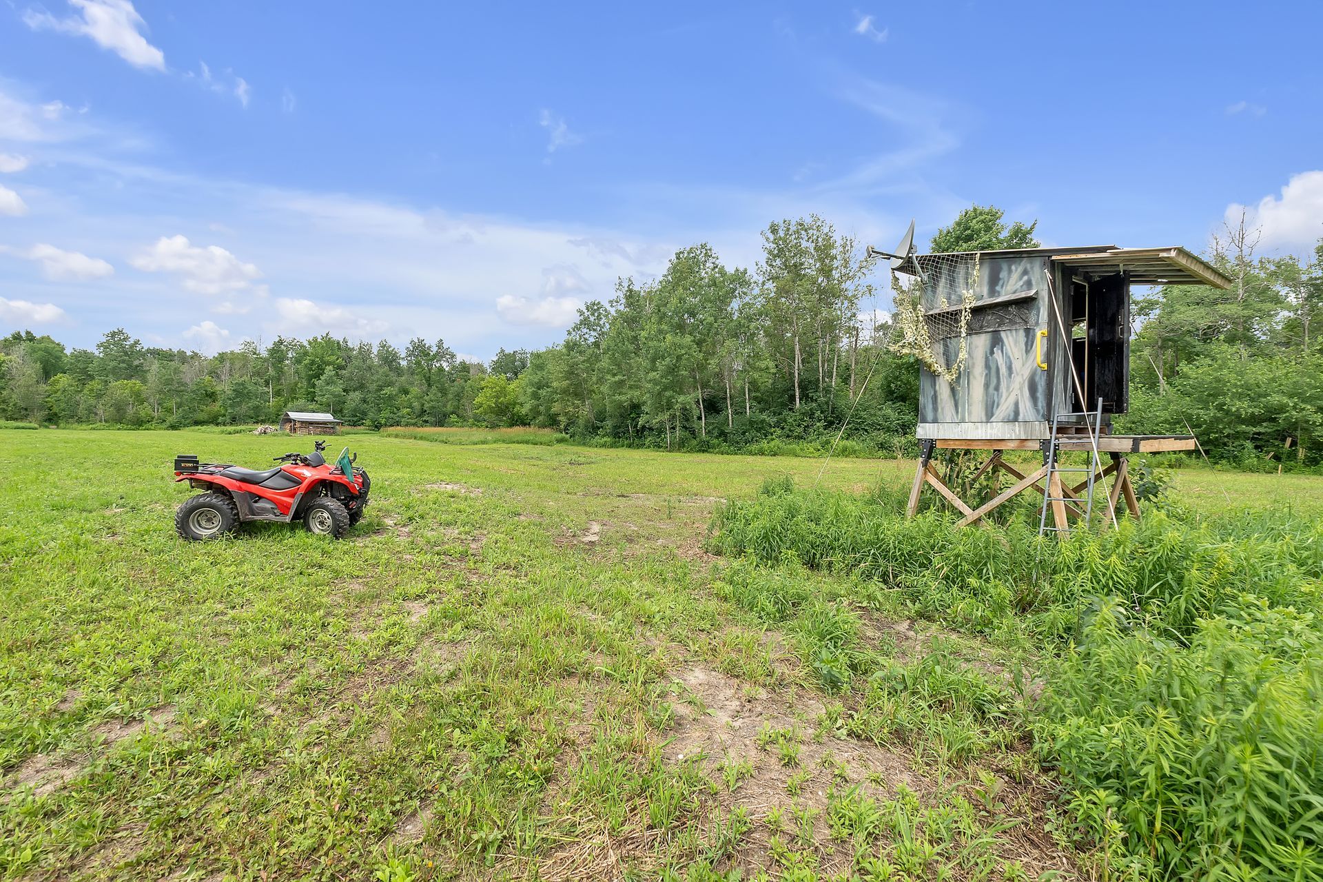 A red atv is parked in a grassy field next to a shed.