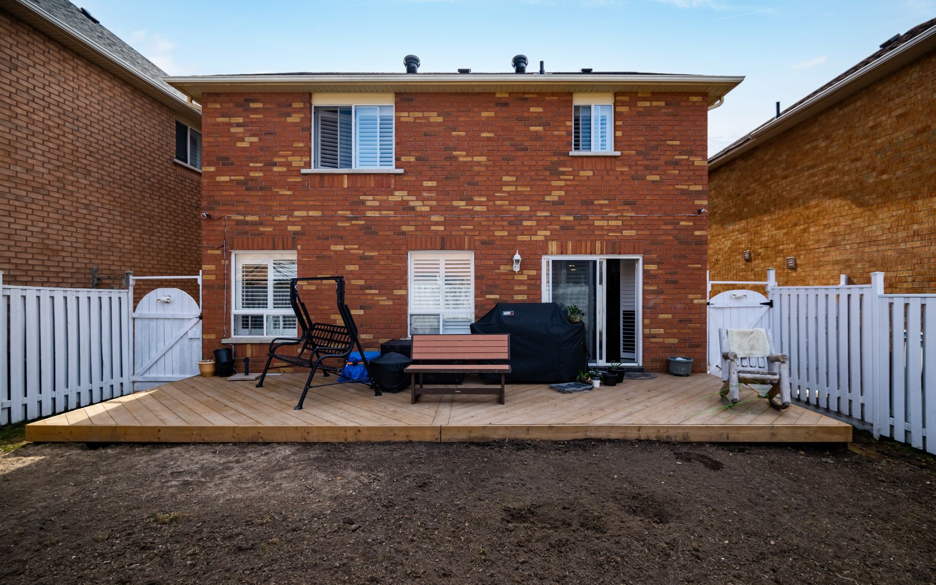 The backyard of a brick house with a wooden deck and fence.