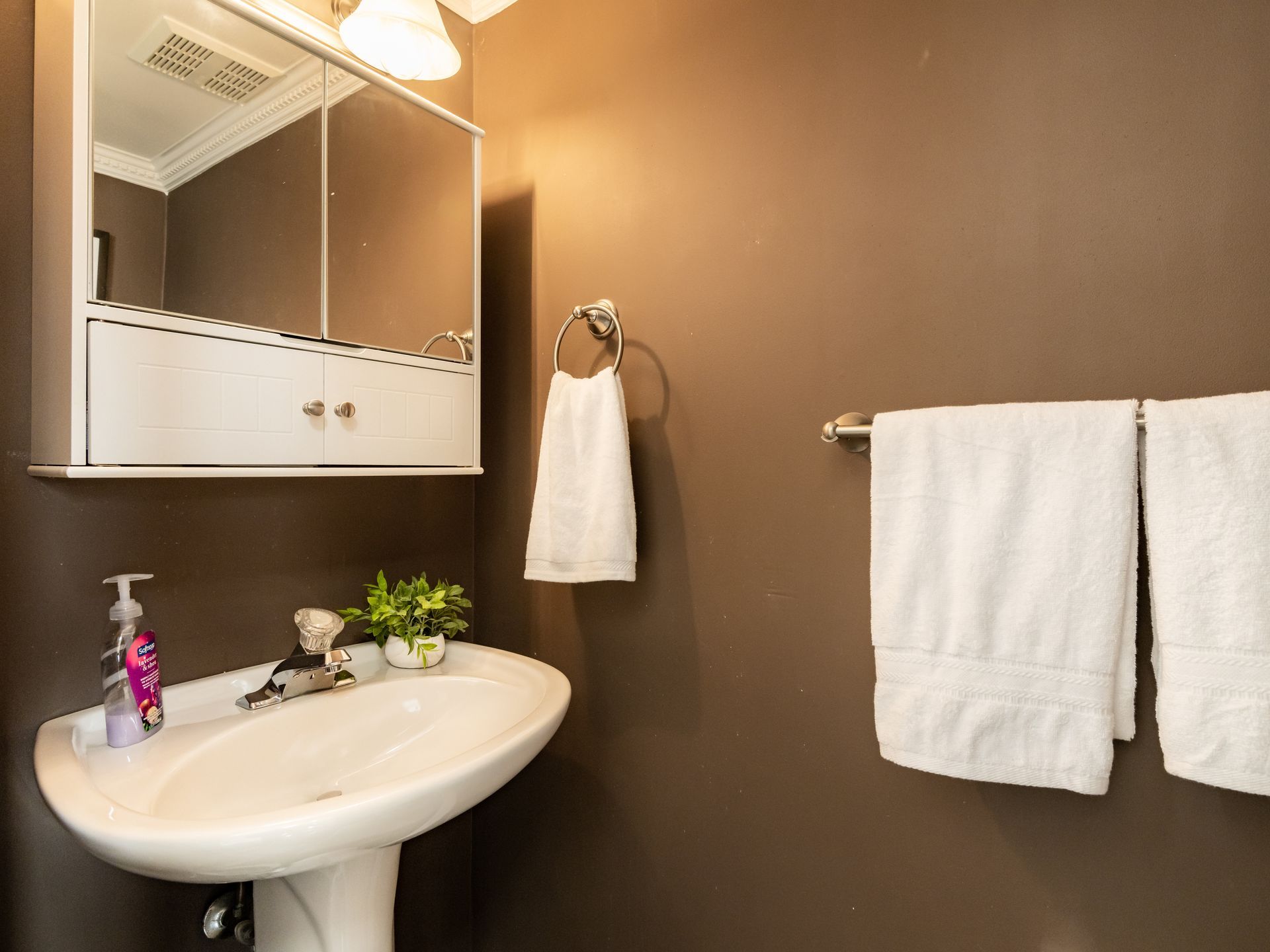 A bathroom with a sink , mirror , and towels hanging on the wall.