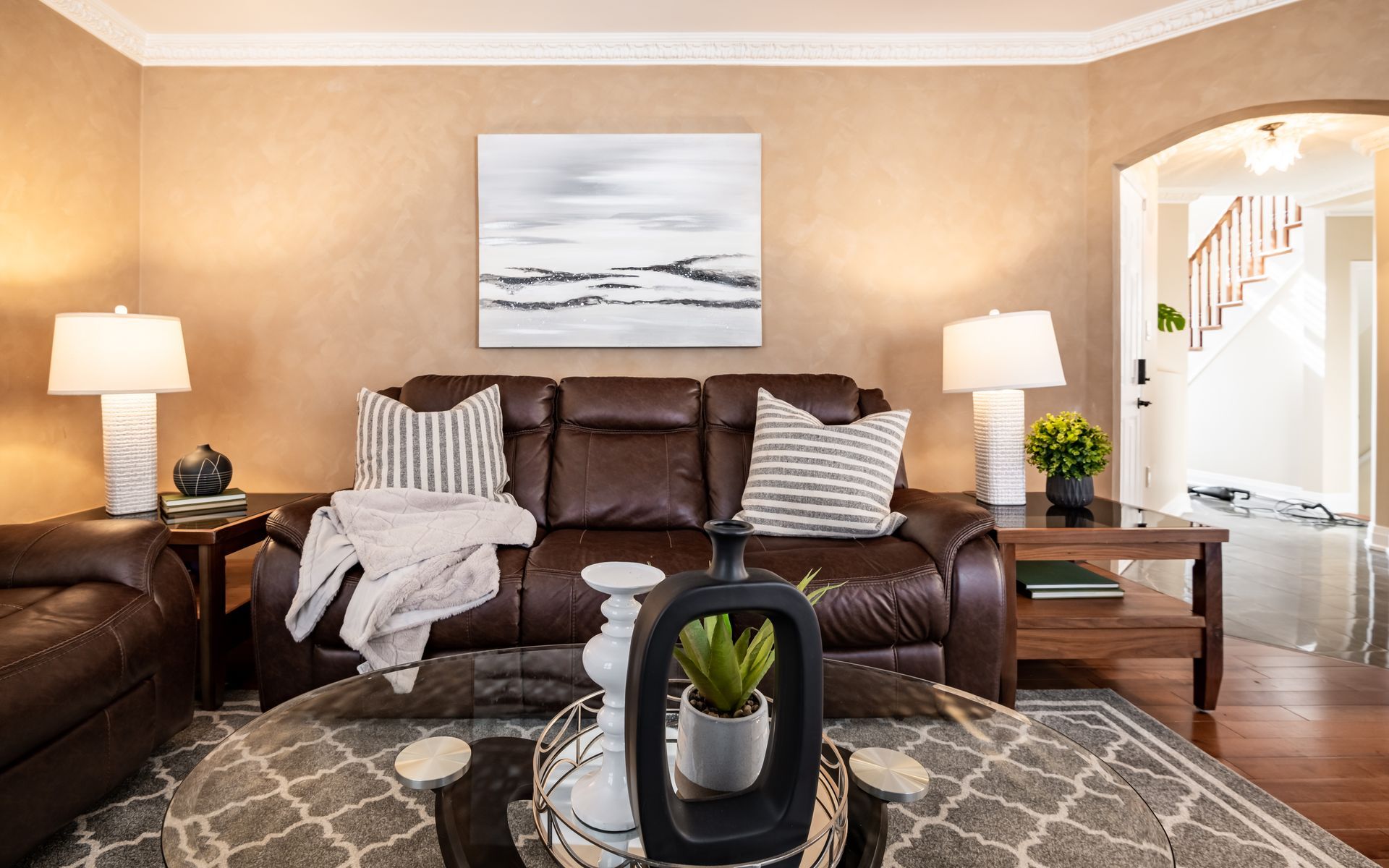 A living room with a brown leather couch , two couches , a coffee table , and a painting on the wall.