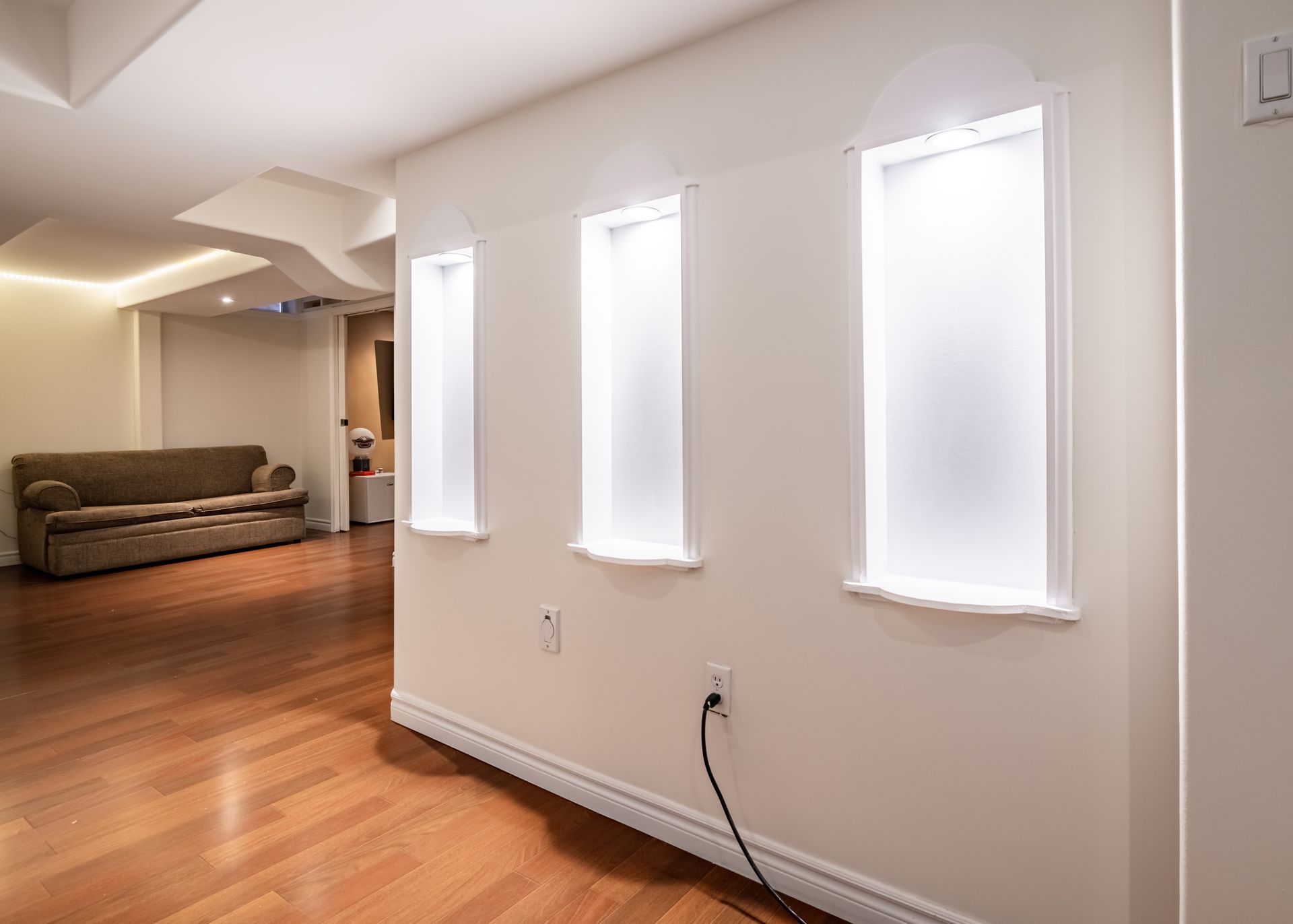 A living room with hardwood floors , a couch , and three windows.