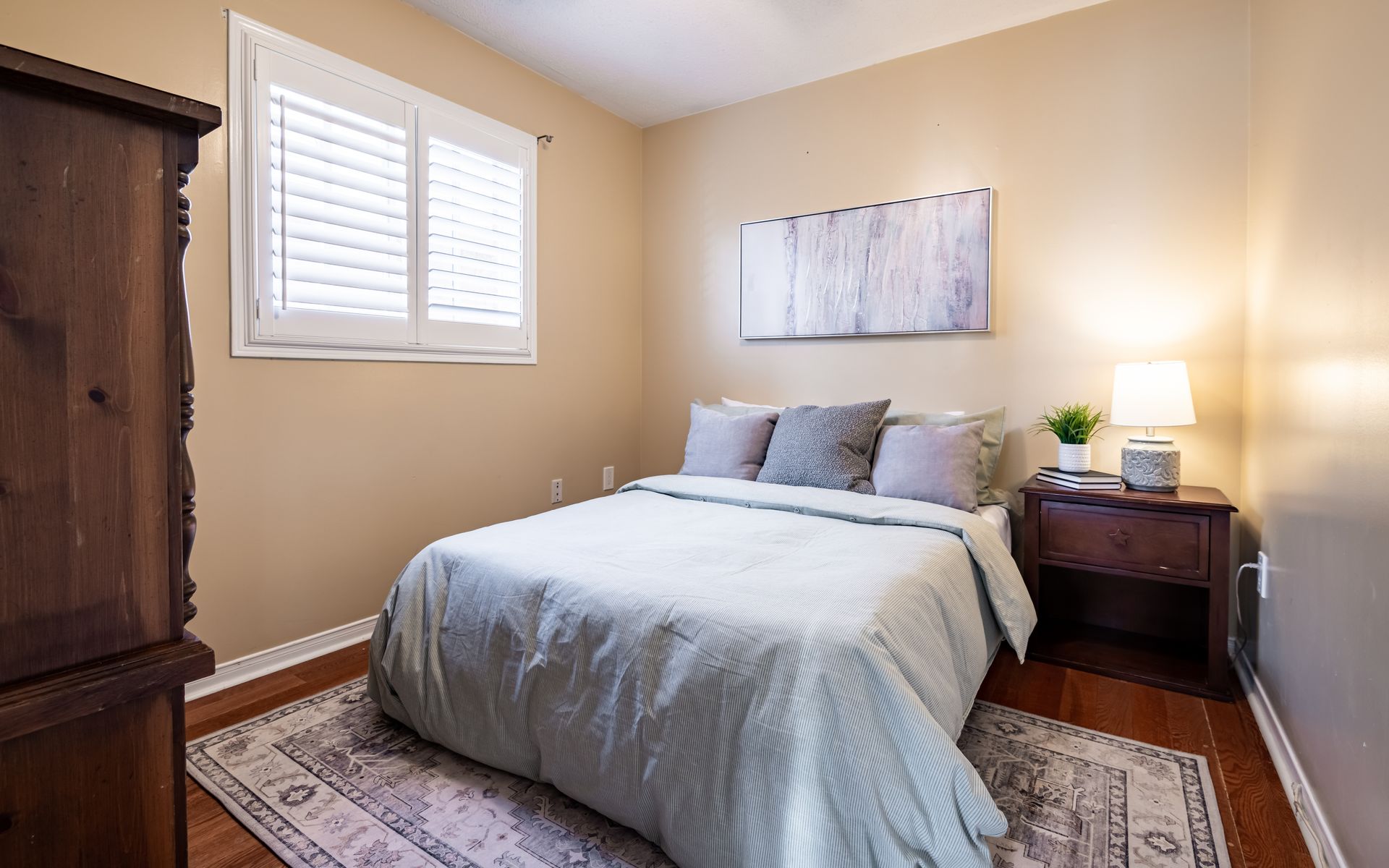 A bedroom with a bed , nightstand , dresser and window.