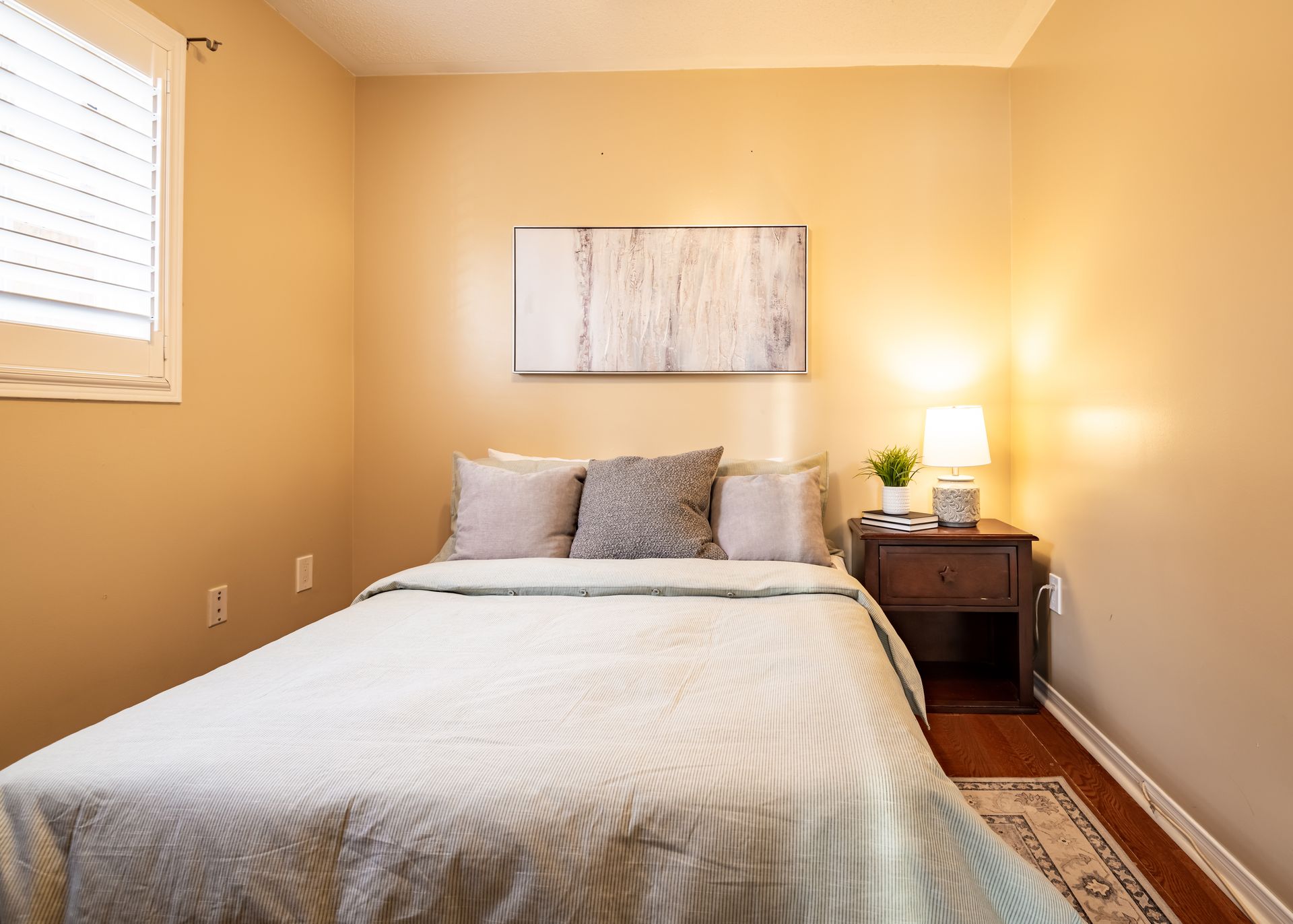 A bedroom with a bed , nightstand , lamp and window.